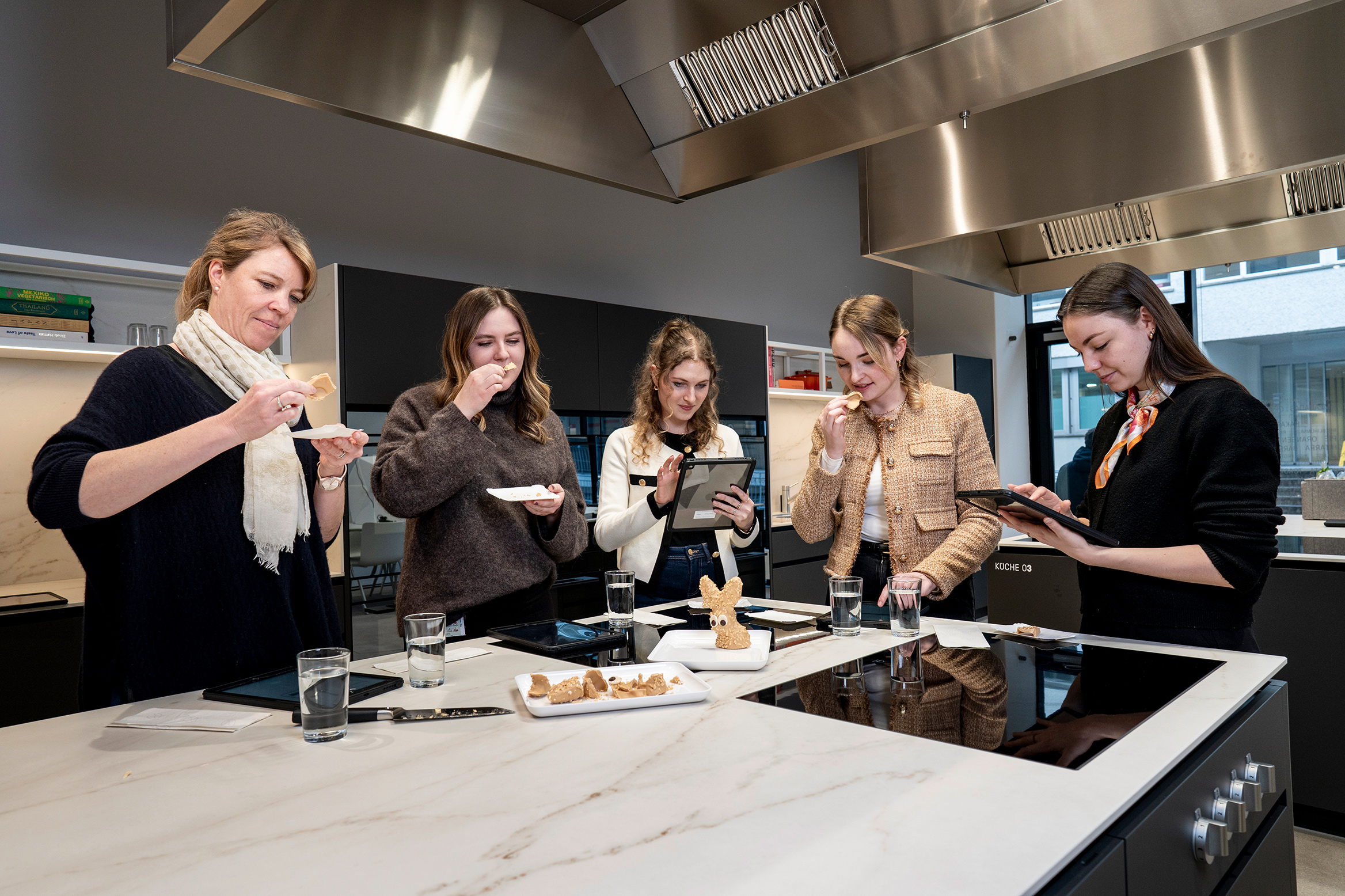 Five female employees are examining a chocolate bunny for appearance and taste.