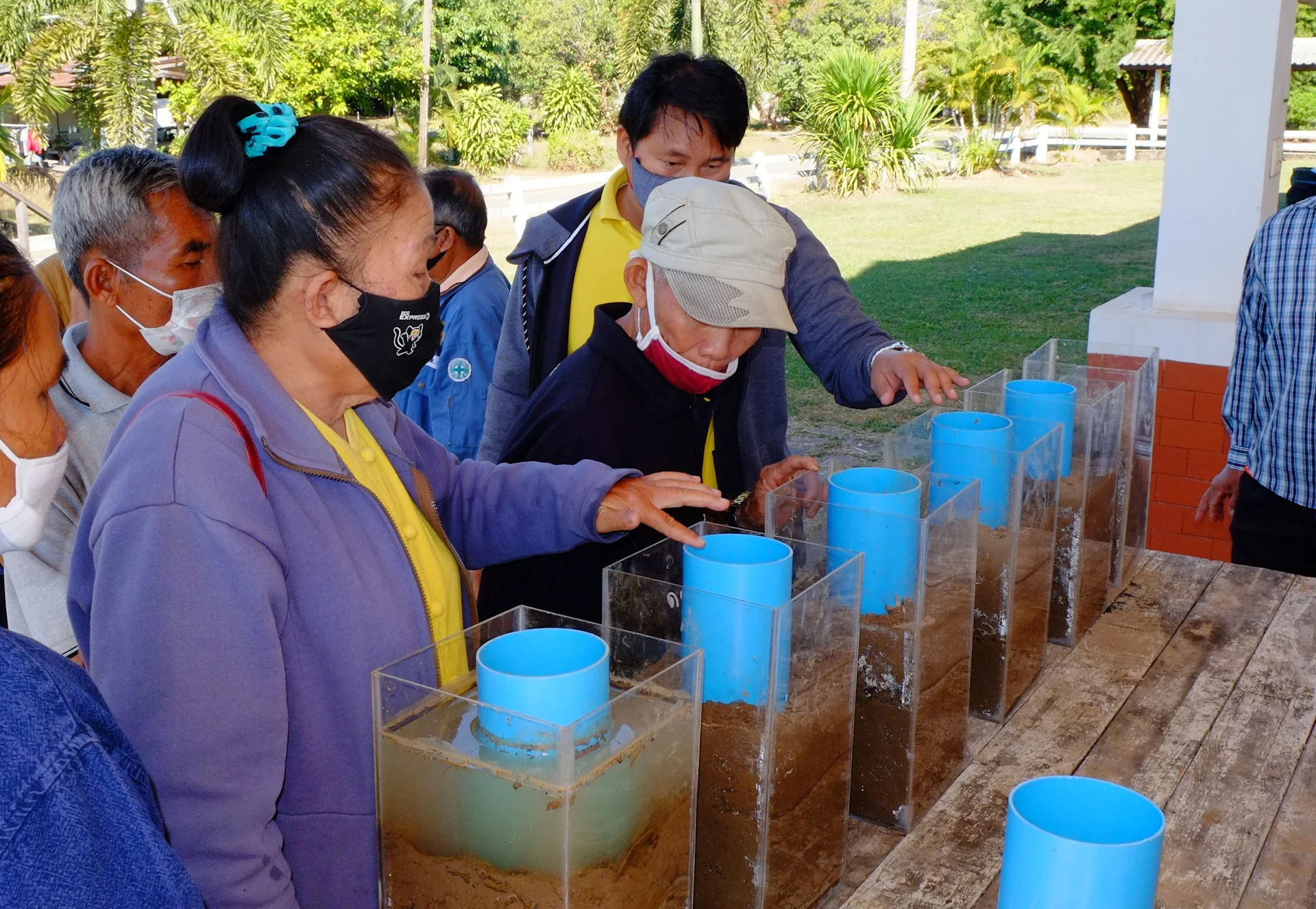 Agricoltori thailandesi osservano i contenitori trasparenti pieni di acqua e terra.