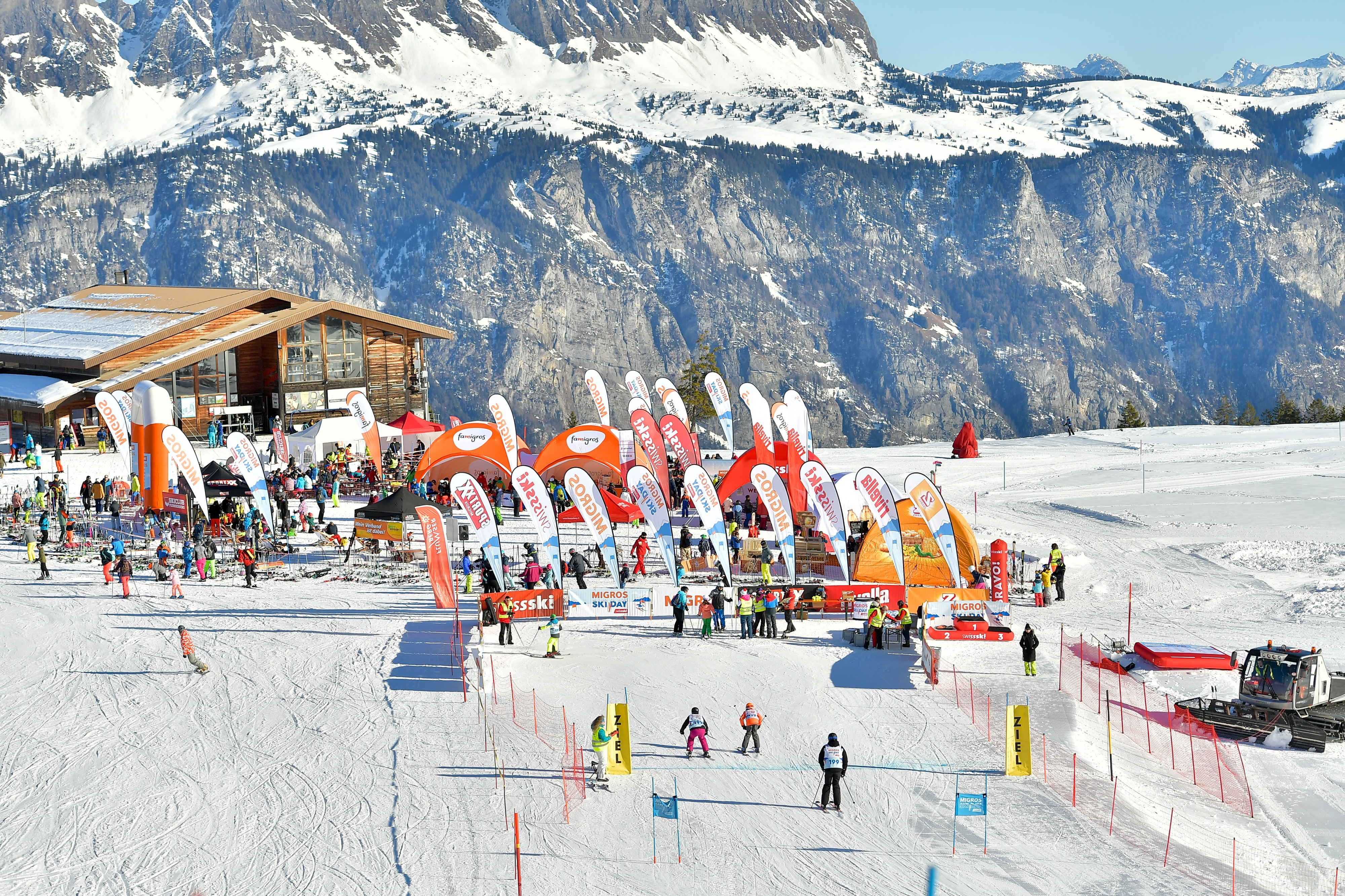 Traguardo di una discesa durante il Migros Ski Day presso una capanna alpina di fronte a un panorama montano.