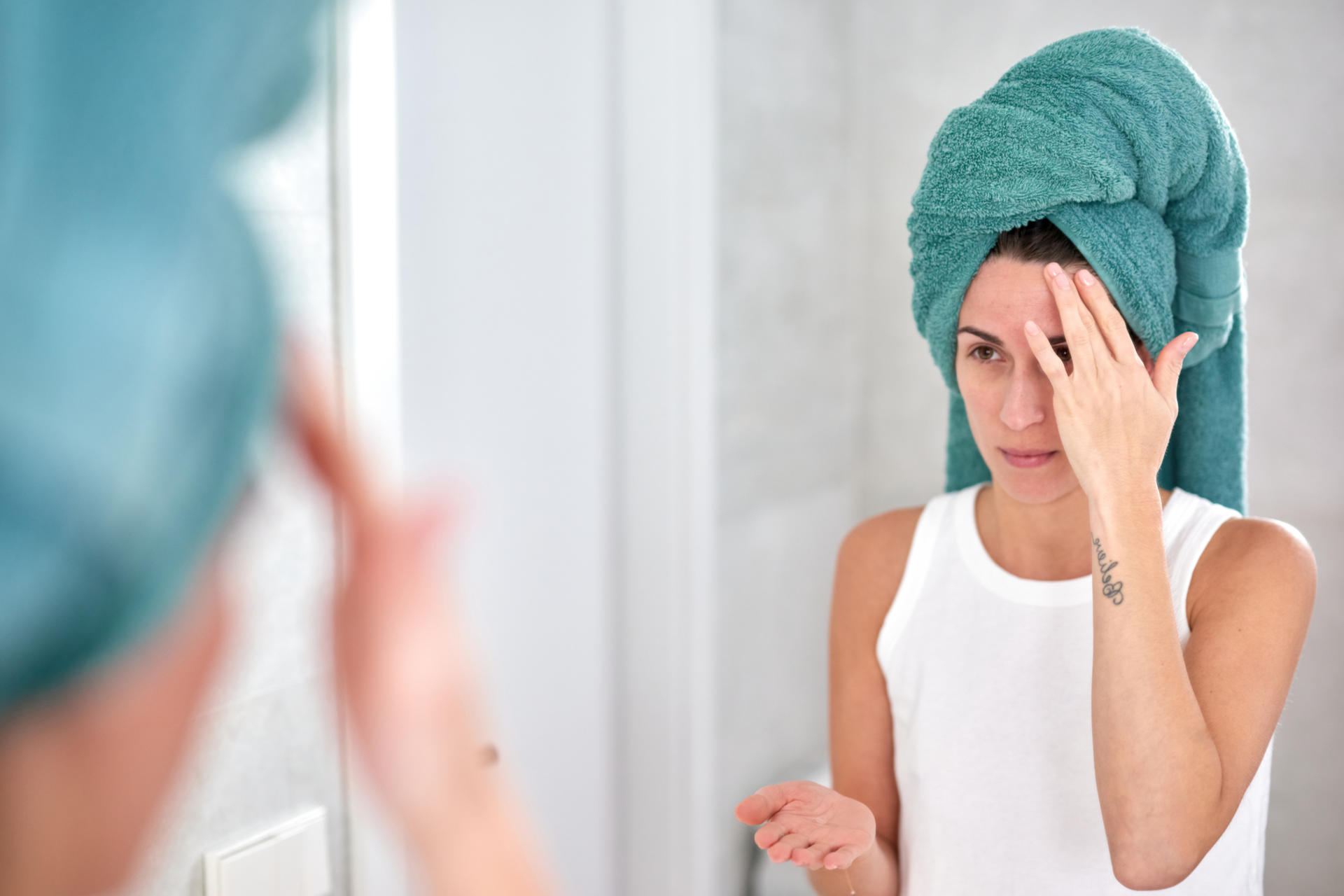 A woman looks at herself in the mirror and applies cream to her face.