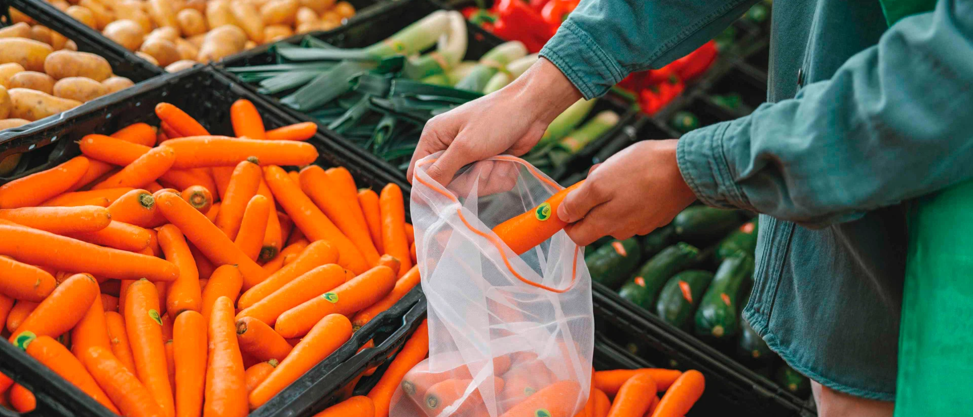A customer puts organic carrots into a reusable vegetable bag.