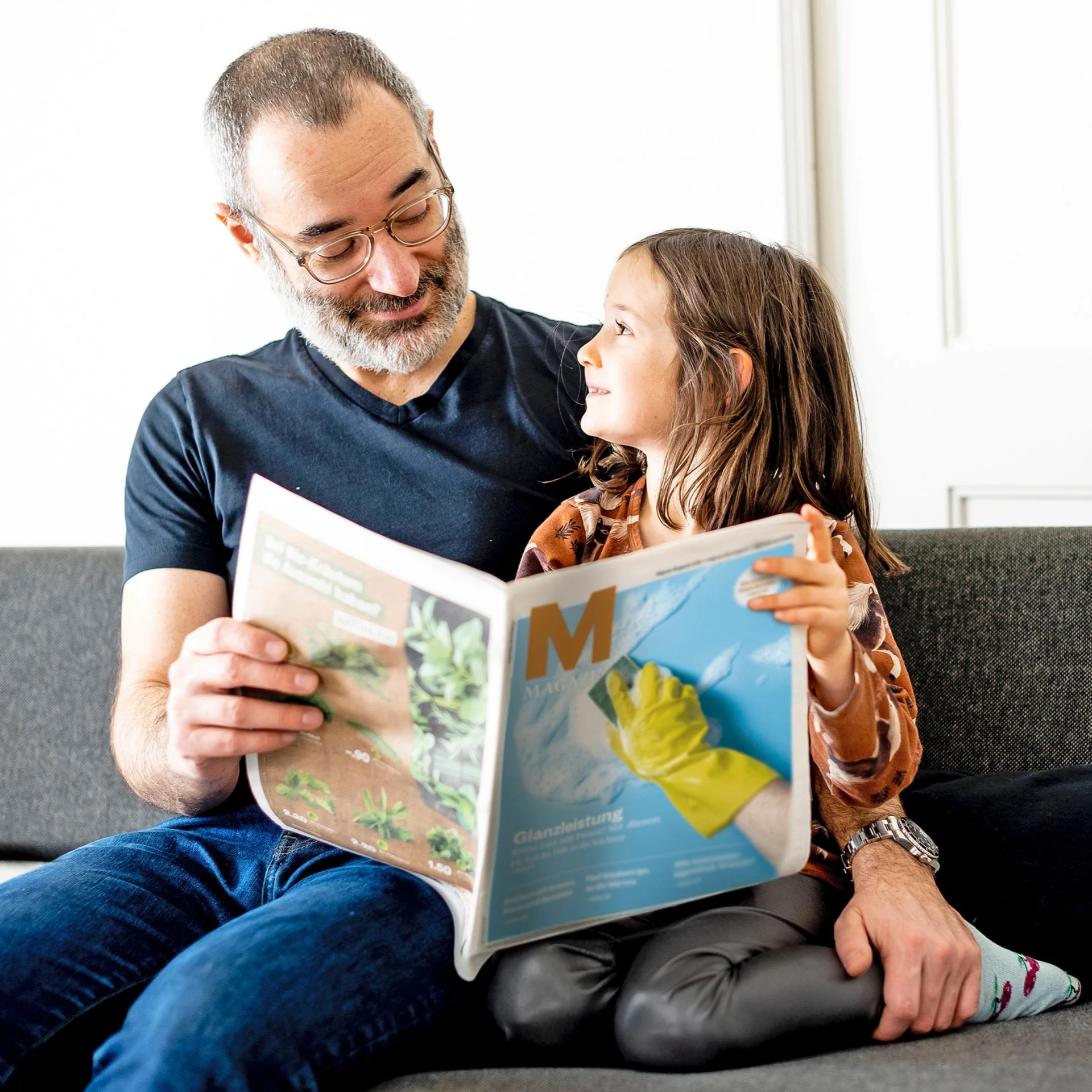 Ein Mann und ein Kind schauen in ein Migros Magazin