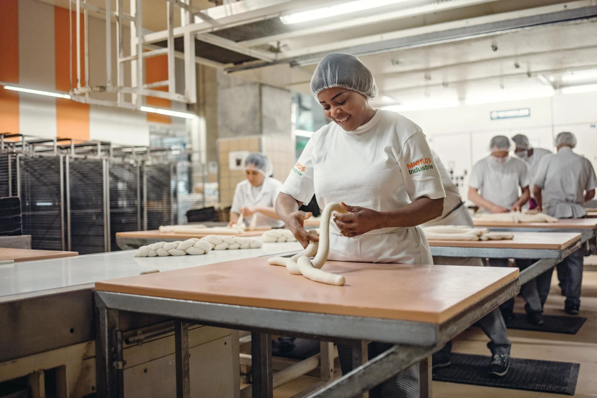 Eine Mitarbeiterin in der Bäckerei formt ein Zopf