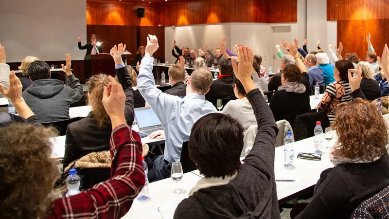 Männer und Frauen strecken die Hände in die Höhe für die Abstimmung im Genossenschaftsrat.