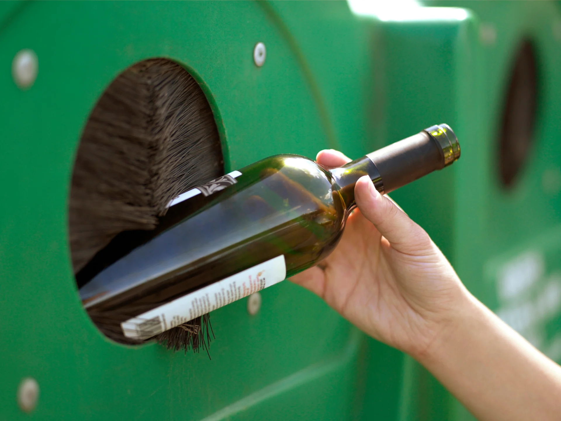 A hand puts a green bottle in a glass trash bin