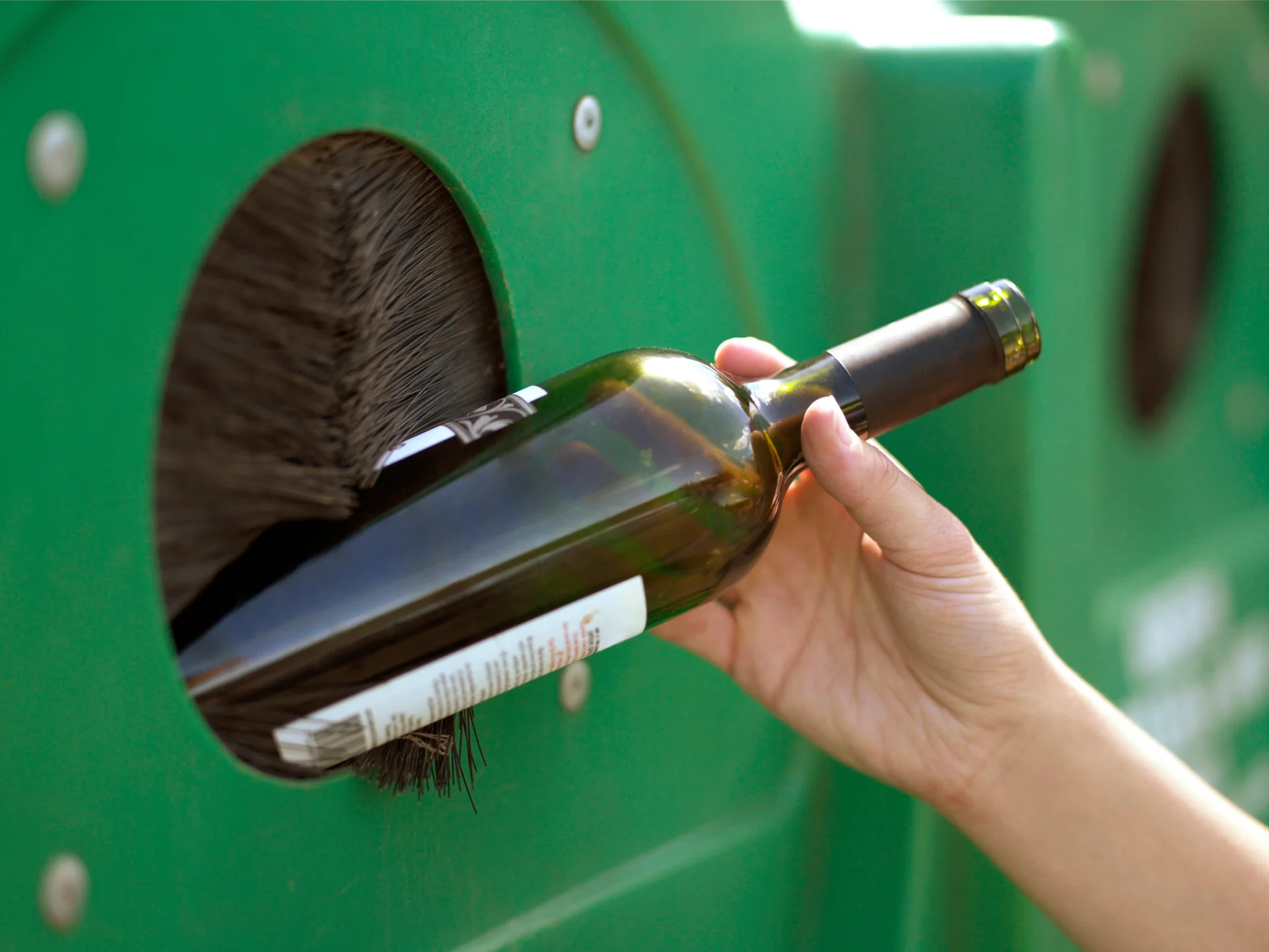 A hand puts a green bottle in a glass trash bin