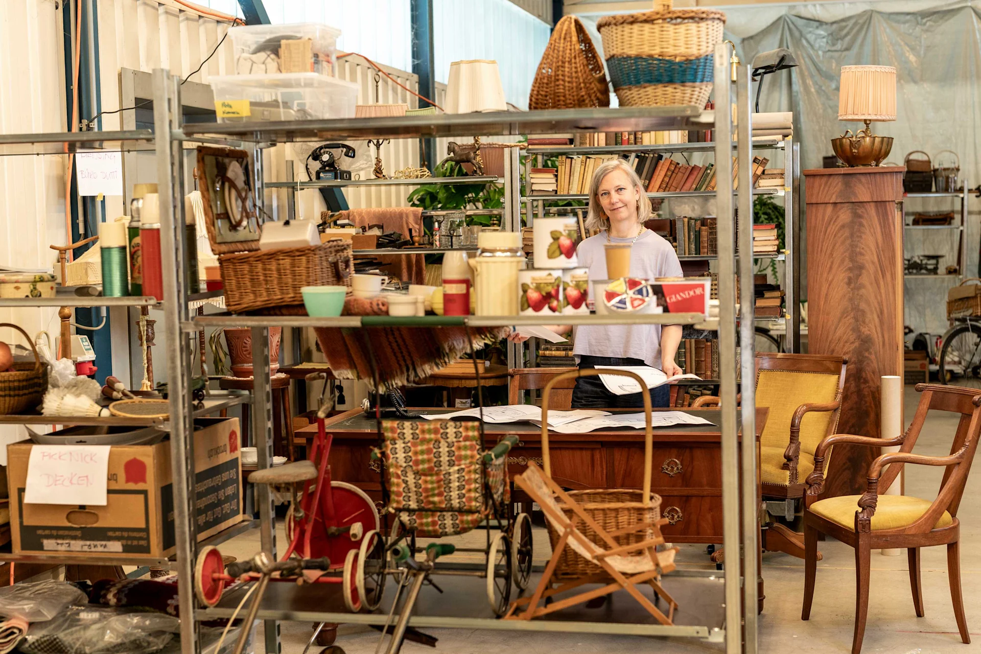 Sue Erdt steht in der Lagerhalle zwischen Regalen, die mit historischen Requisiten gefüllt sind
