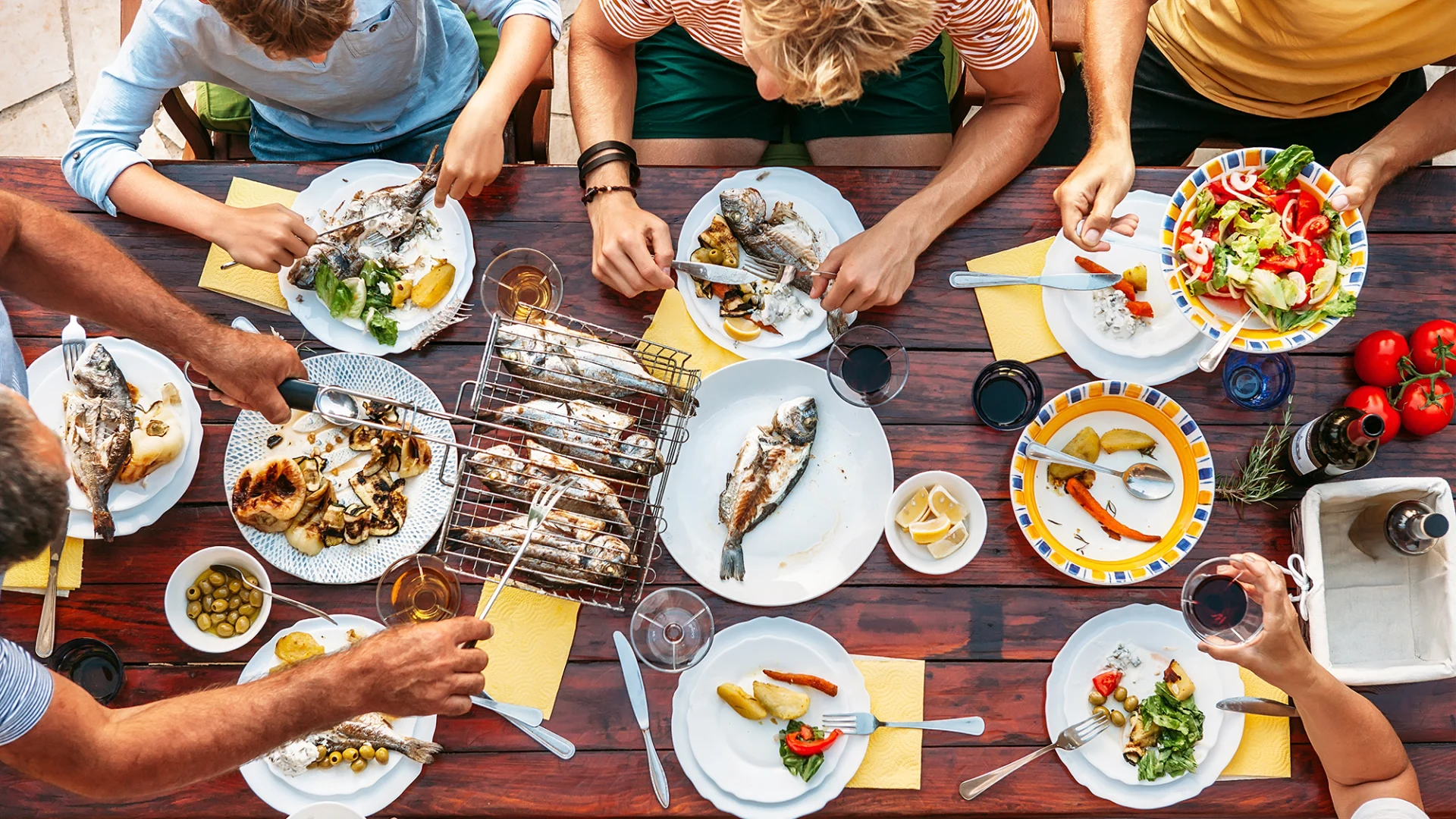 Cinque persone sedute a un tavolo si gustano delle pietanze cotte alla griglia.