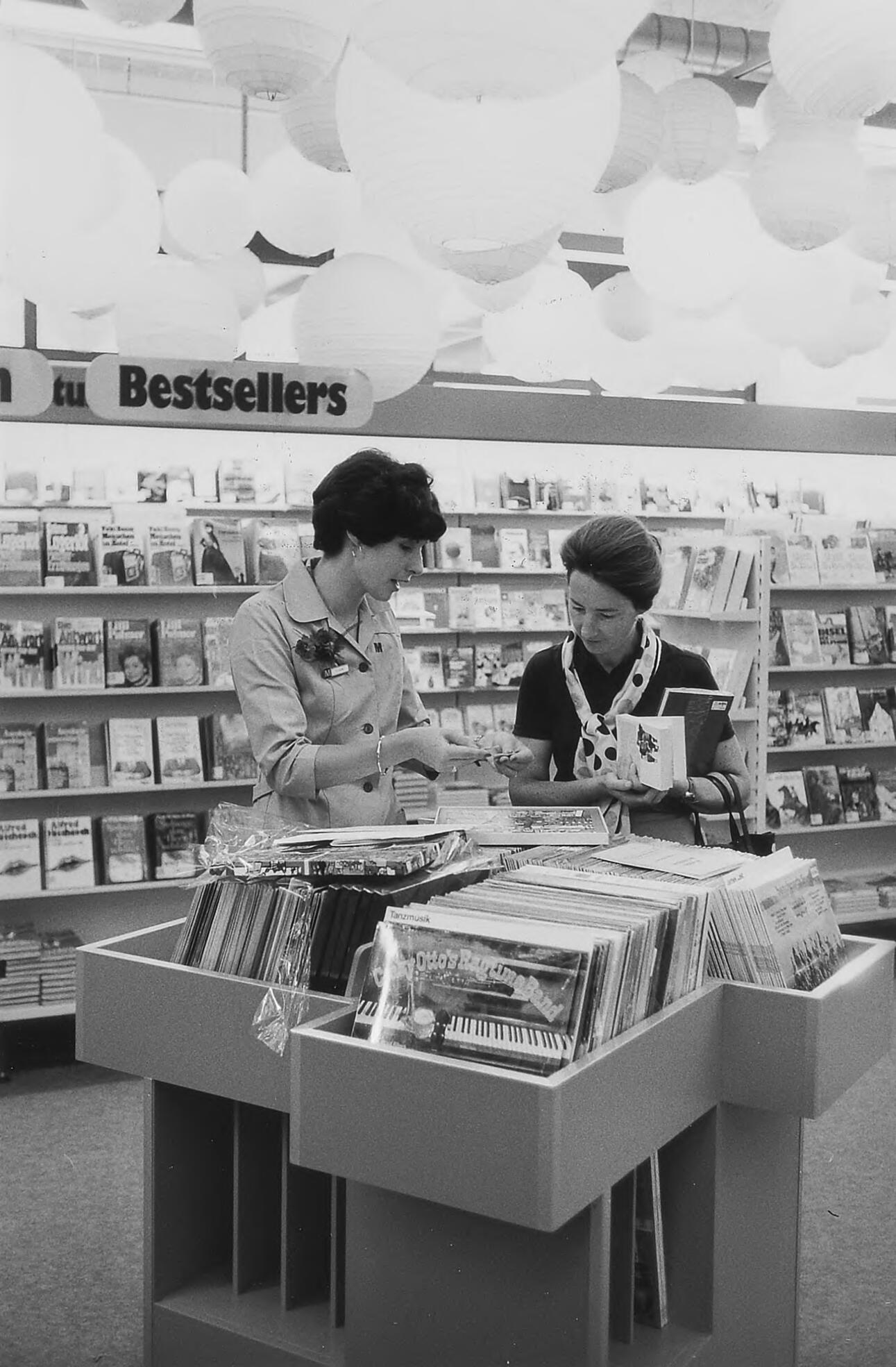 A black-and-white photograph of a saleswoman and a customer in a record shop
