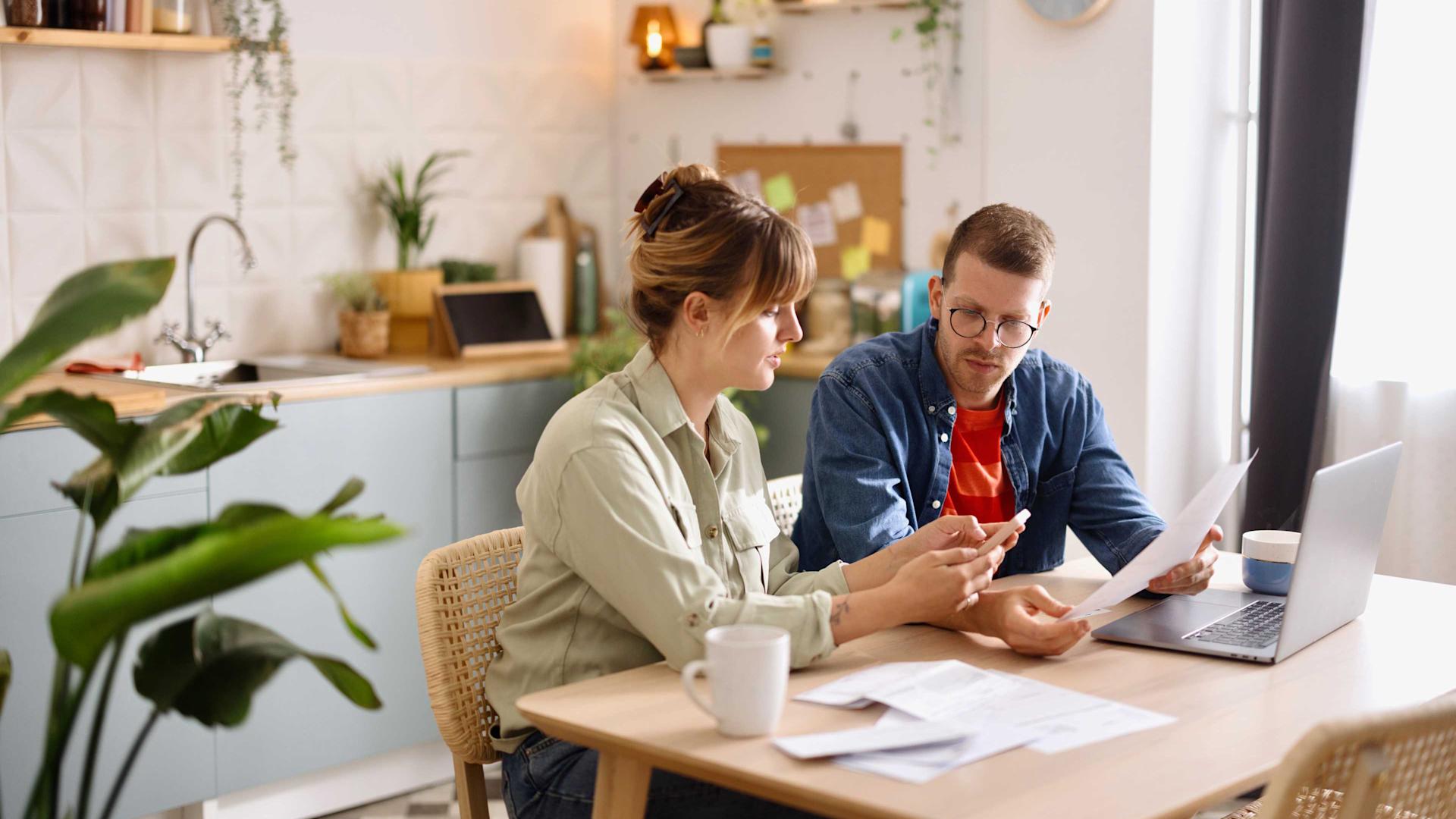 Una giovane donna e un giovane uomo pagano le bollette al tavolo della cucina
