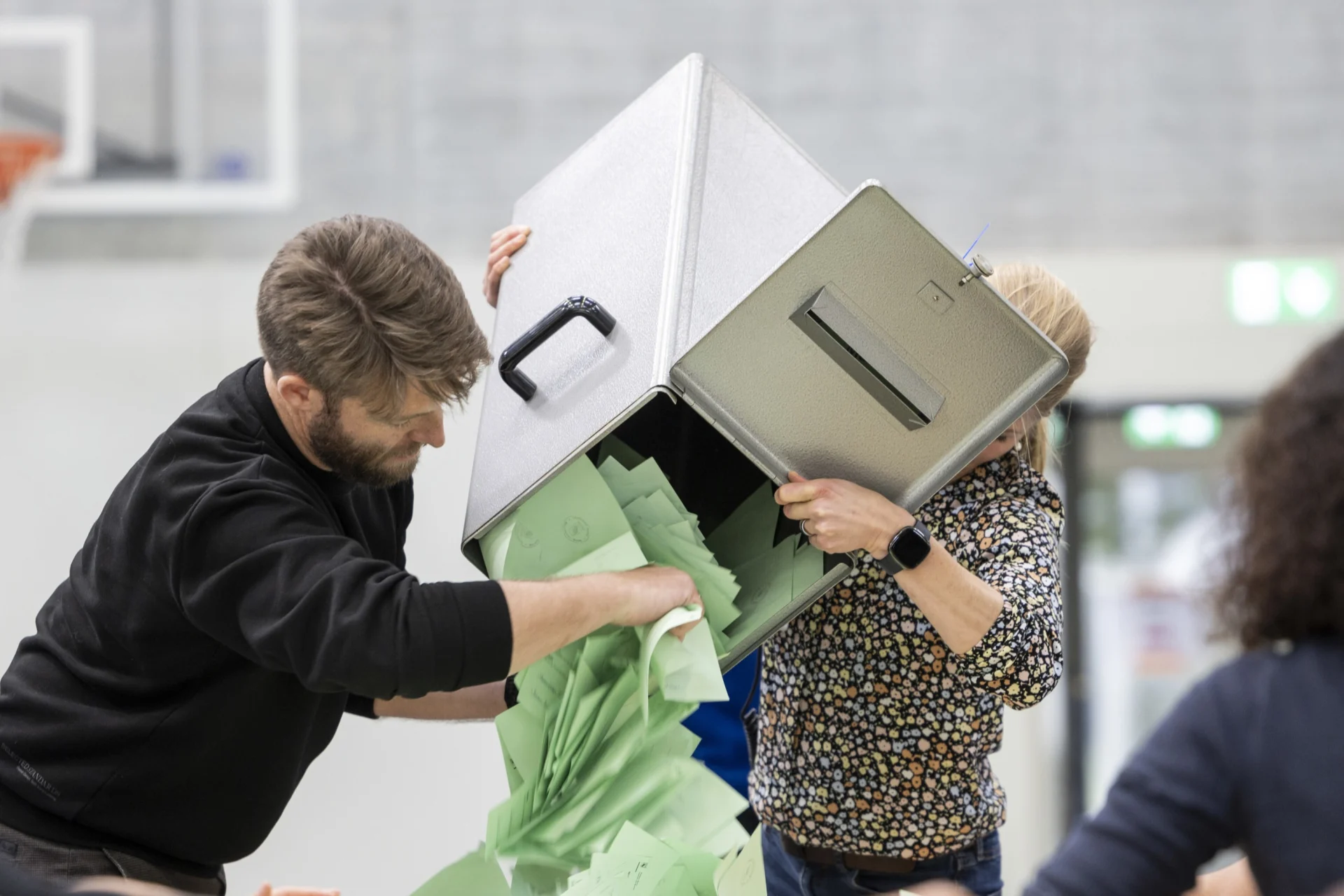 A group of people empty a voting box with voting slips onto a table.
