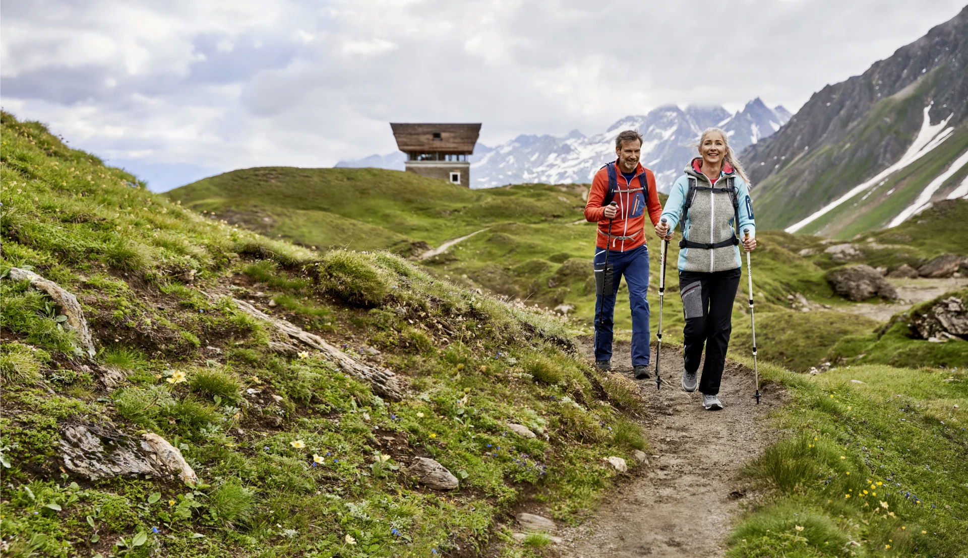 Una coppia cammina con i bastoncini da trekking su un sentiero di montagna.
