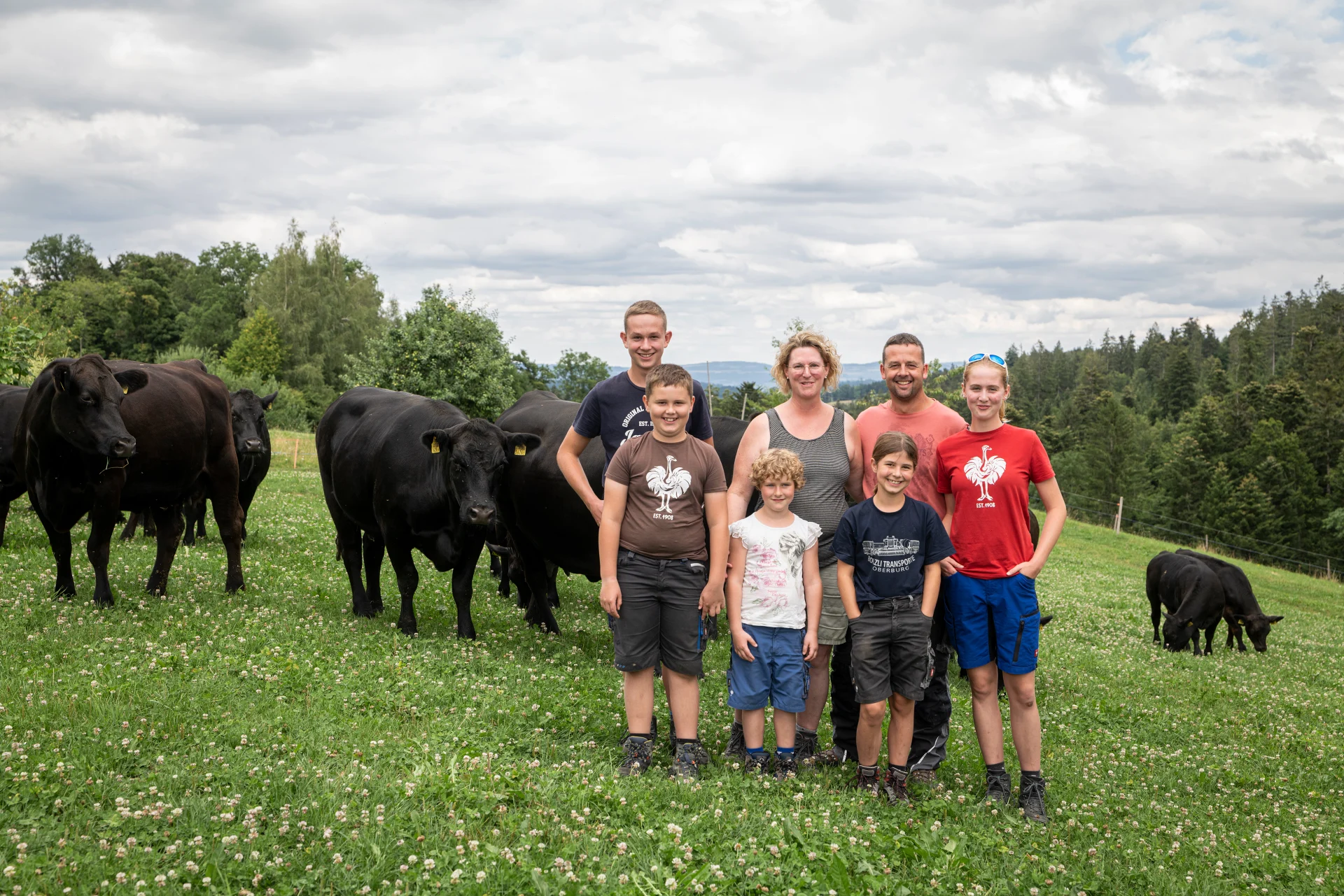 The Röthlisberger family stands in front of the cattle in the pasture.