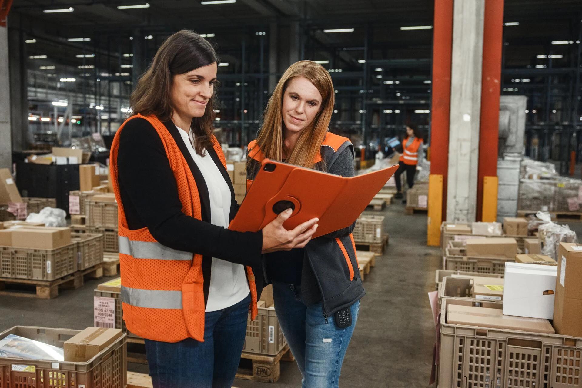 Two employees use a tablet computer together in a large warehouse.