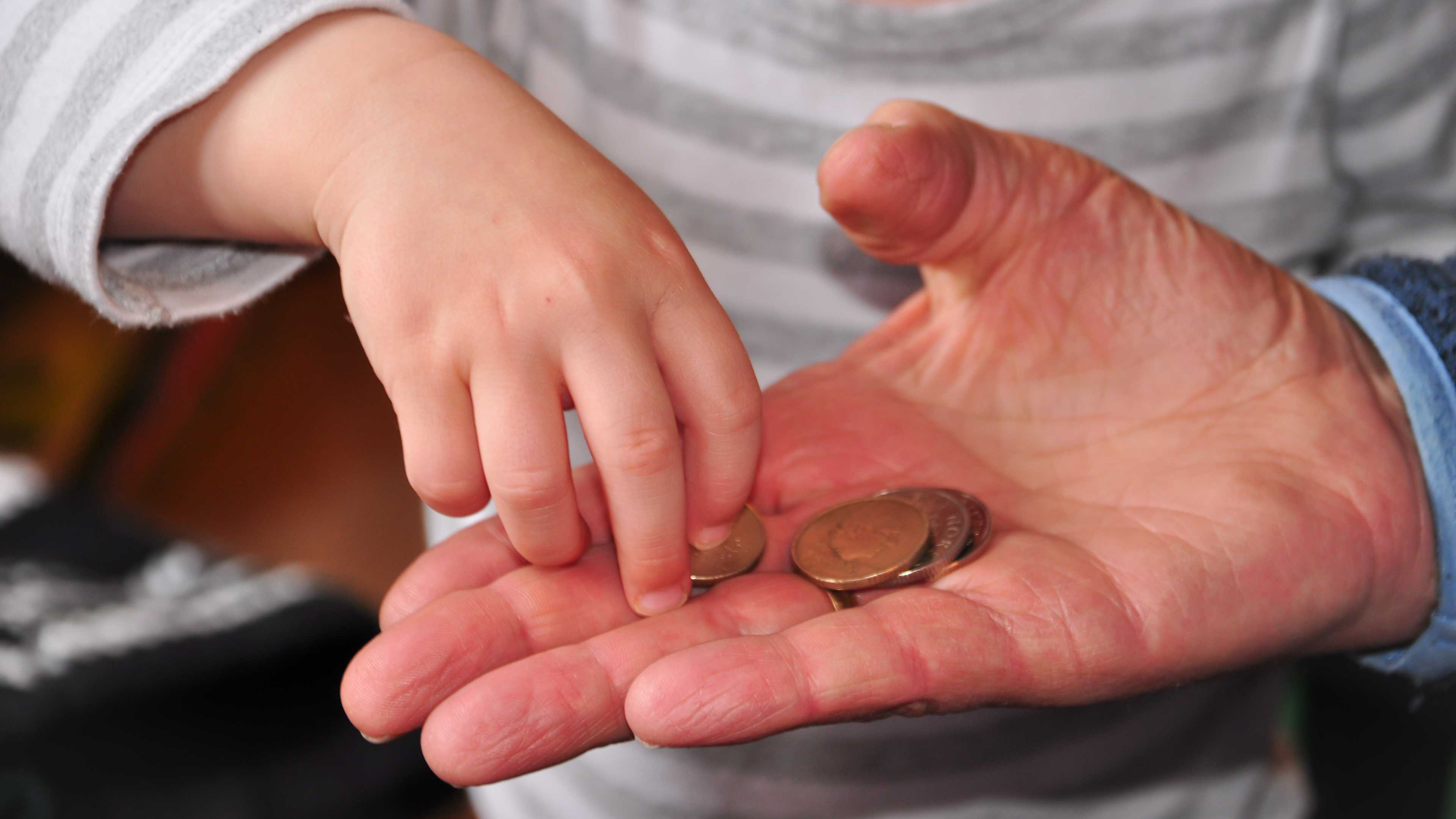 Un bambino tocca le monete nella mano di un uomo