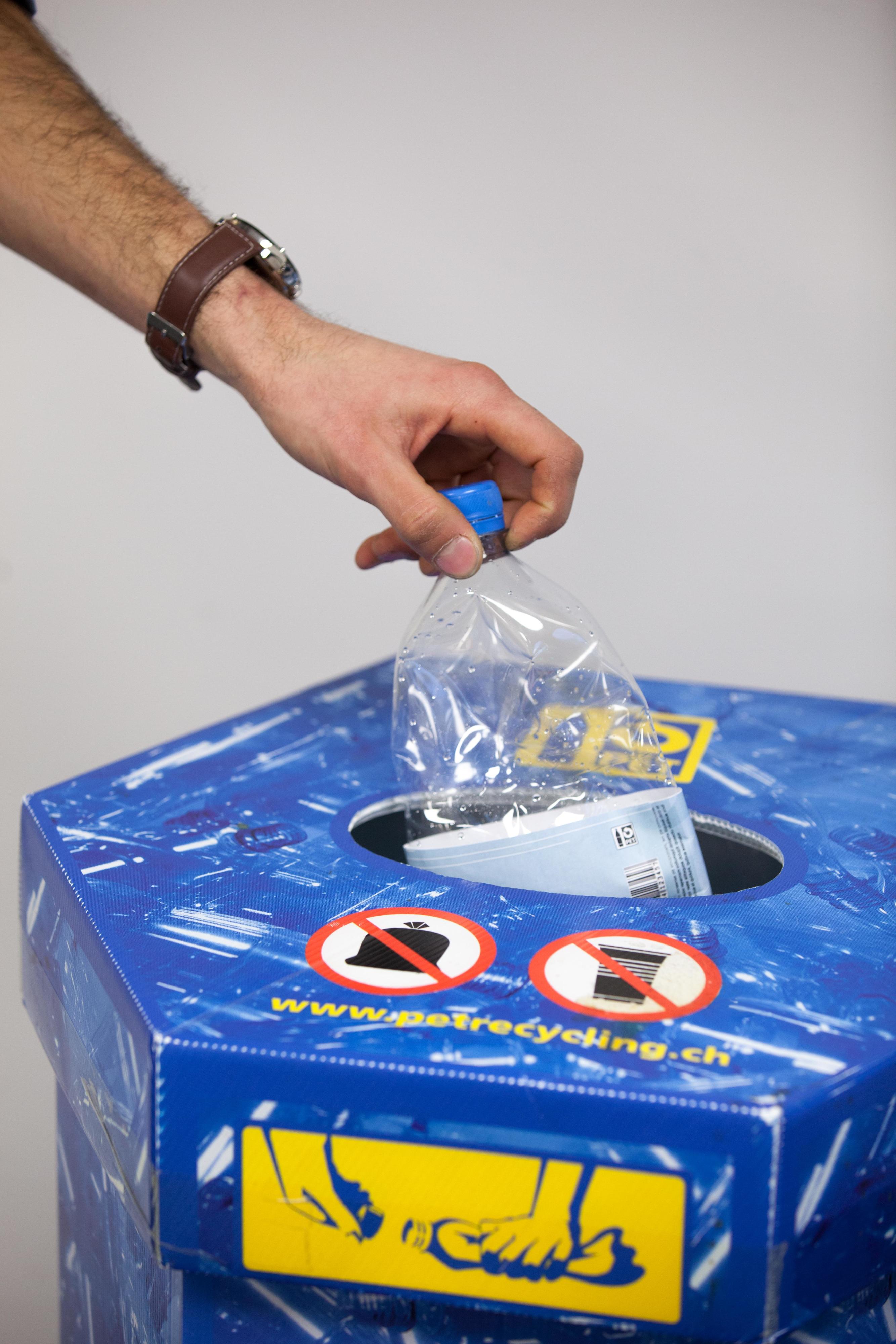 Eine Hand hält eine PET-Flasche in einen Recycling-Behälter