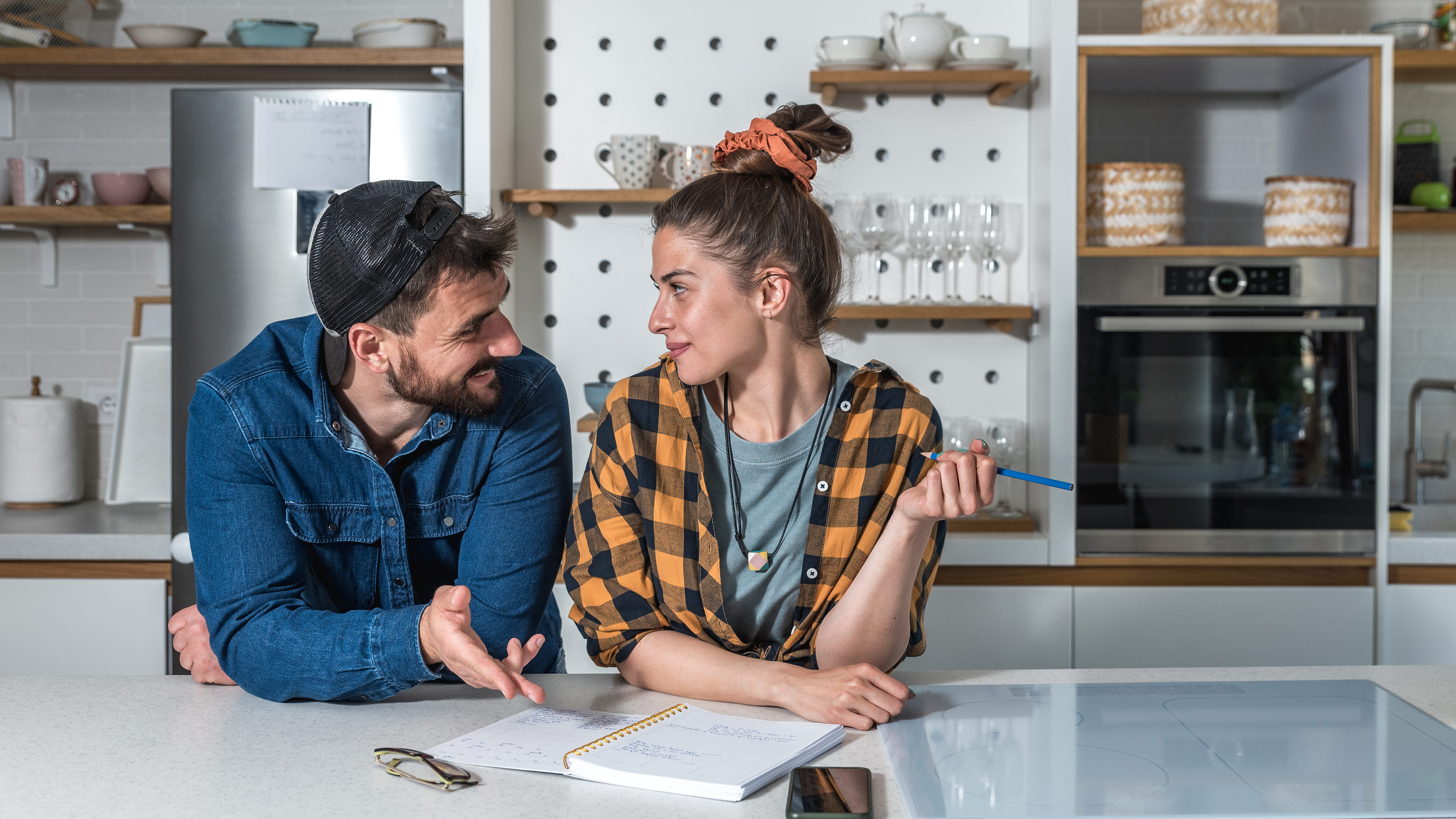 Jeune couple heureux debout dans leur cuisine en train de faire une liste dans un carnet