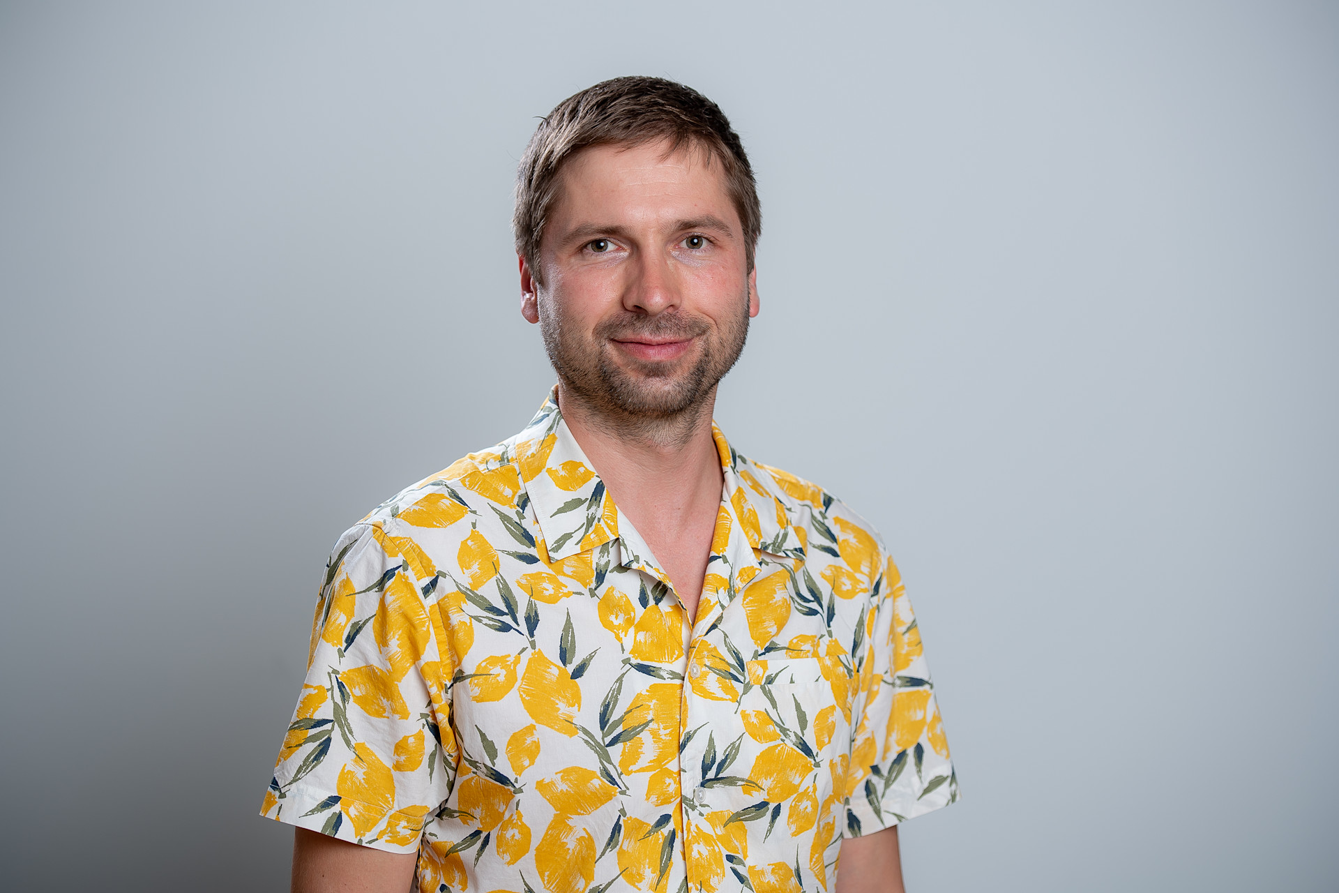 Person in einem sommerlichen gelb‑weissen Hemd mit floralem Muster vor neutralem Hintergrund.