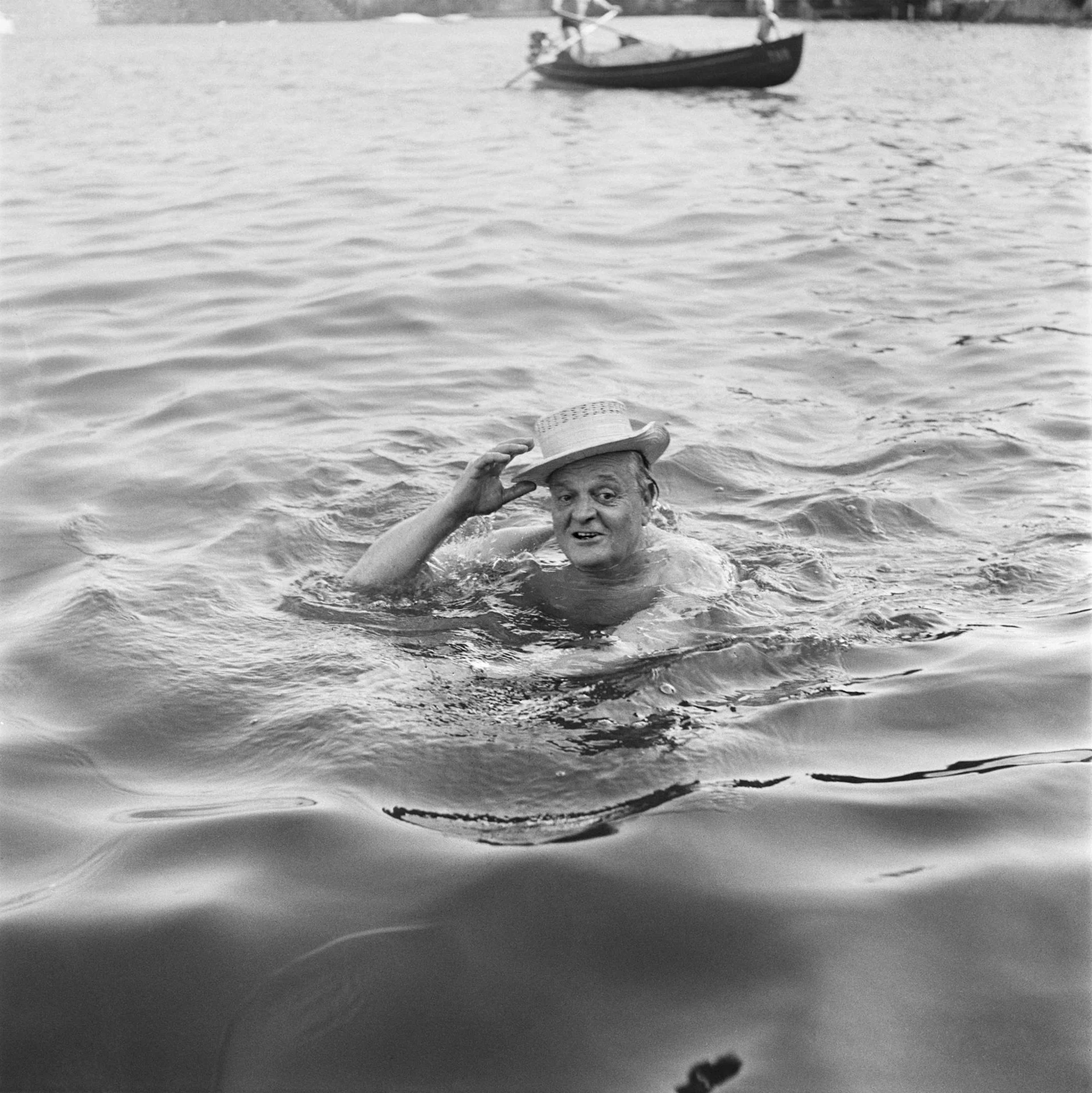 Dutti – geliebt und gehasst Eine Schwarz-Weiss-Fotografie von Gottlieb Duttweiler. Dutti schwimmt im See und trägt einen Hut.
