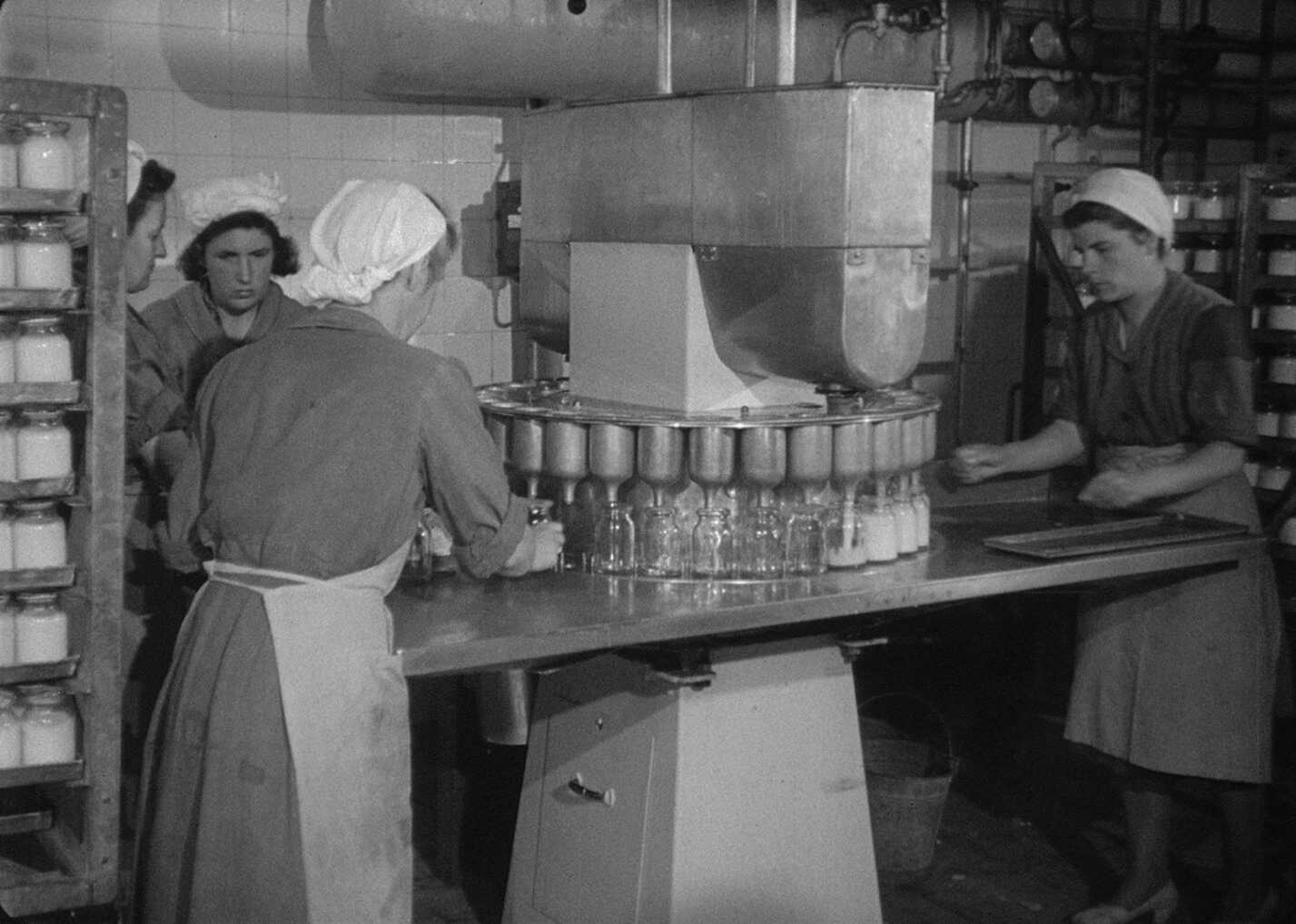 Le donne sono in piedi attorno a una macchina che riempie vasetti di yogurt.