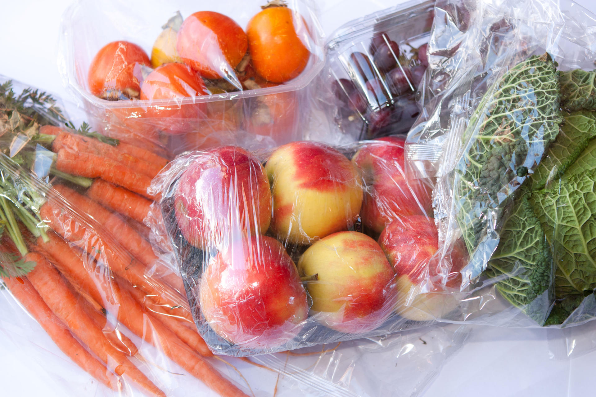 Karotten, Tomaten, Äpfel, Trauben und Kohl in Plastikverpackungen.