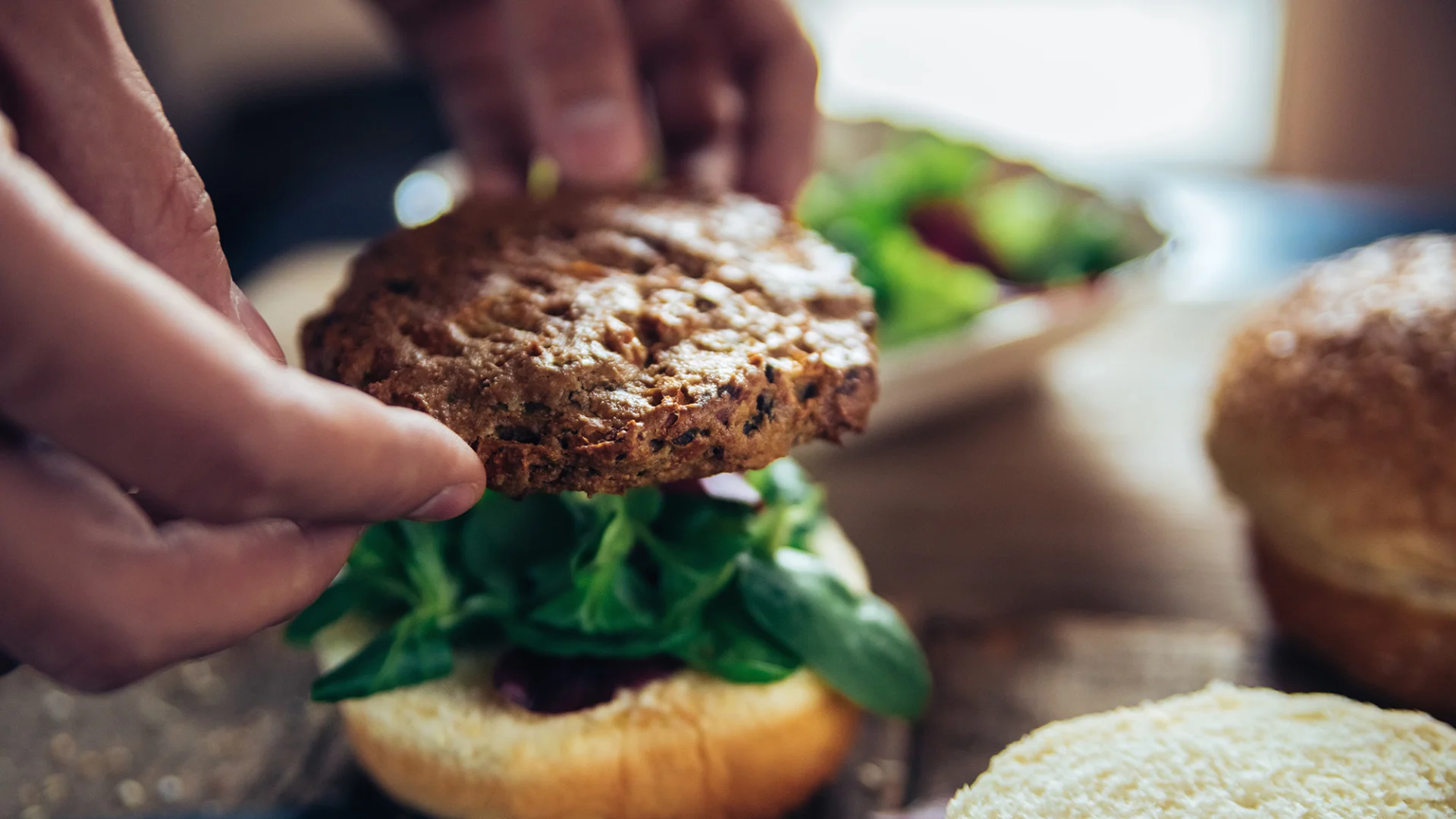 Un burger viene adagiato su un apposito panino con dell'insalata.