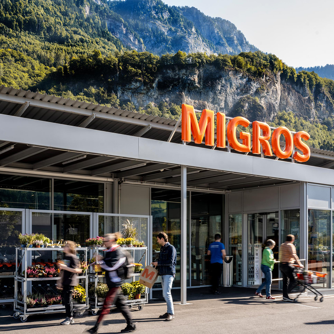 Area esterna di un'attrattiva filiale Migros con montagne sullo sfondo