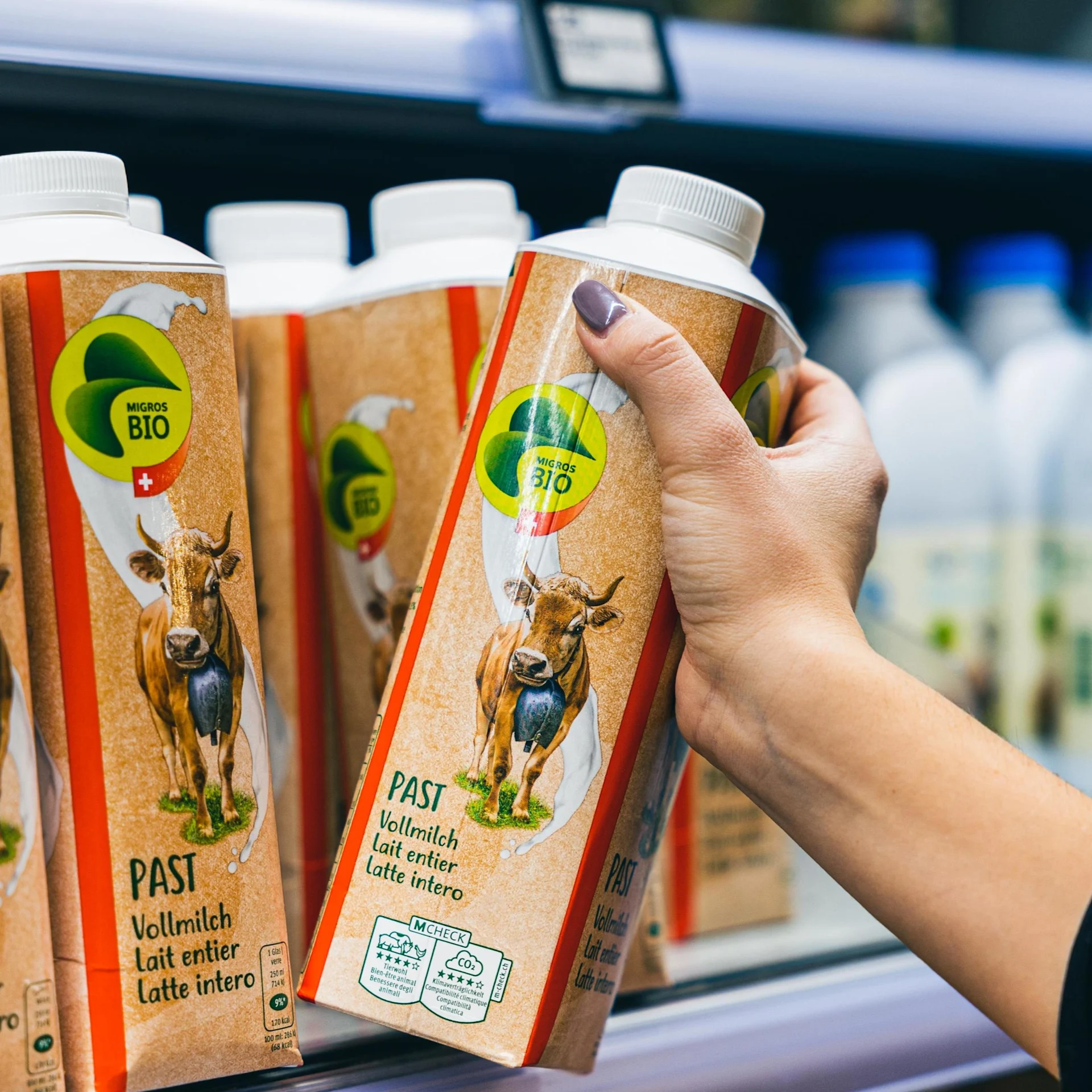 A hand takes a liter bottle of organic whole milk from the shelf ​