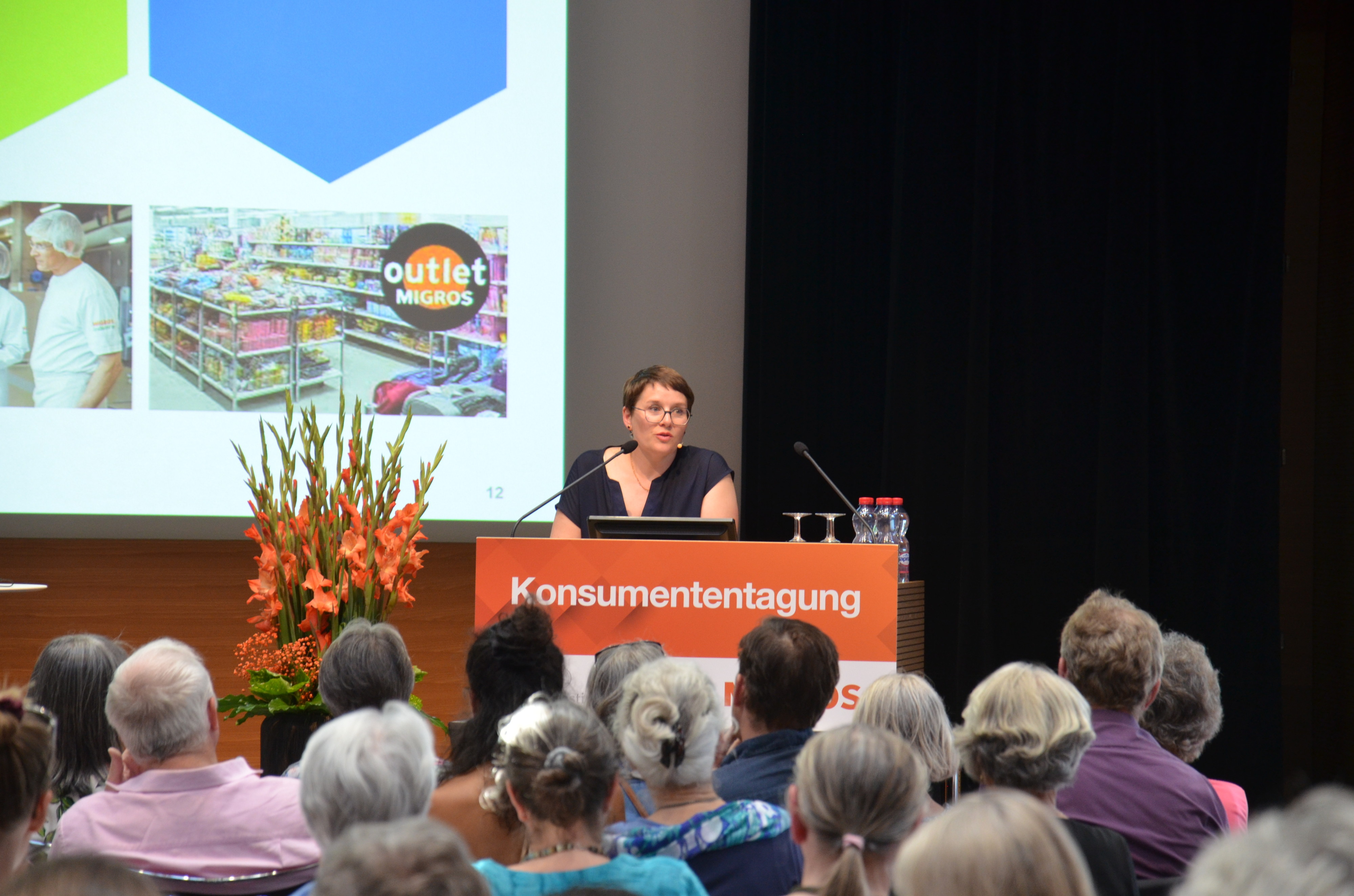 Eine Frau spricht auf der Bühne der Konsumententagung zu einem Publikum.
