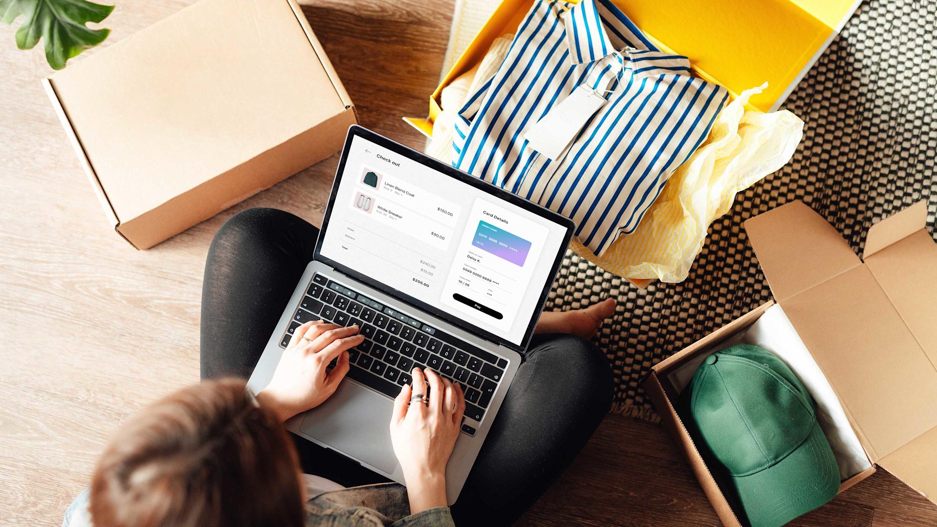 Eine Person sitzt am Boden und gibt am Laptop eine Online-Bestellung auf