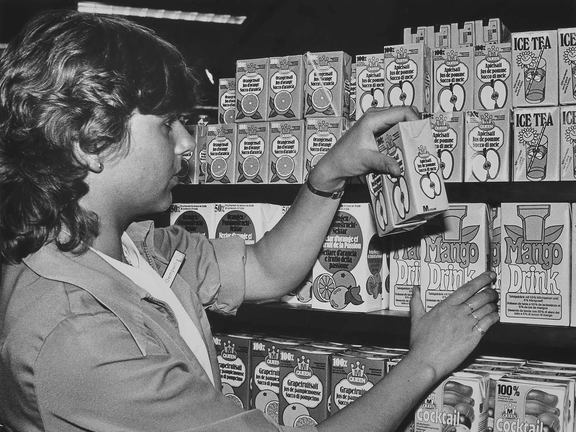 A sales assistant places apple juice on the shop shelf.