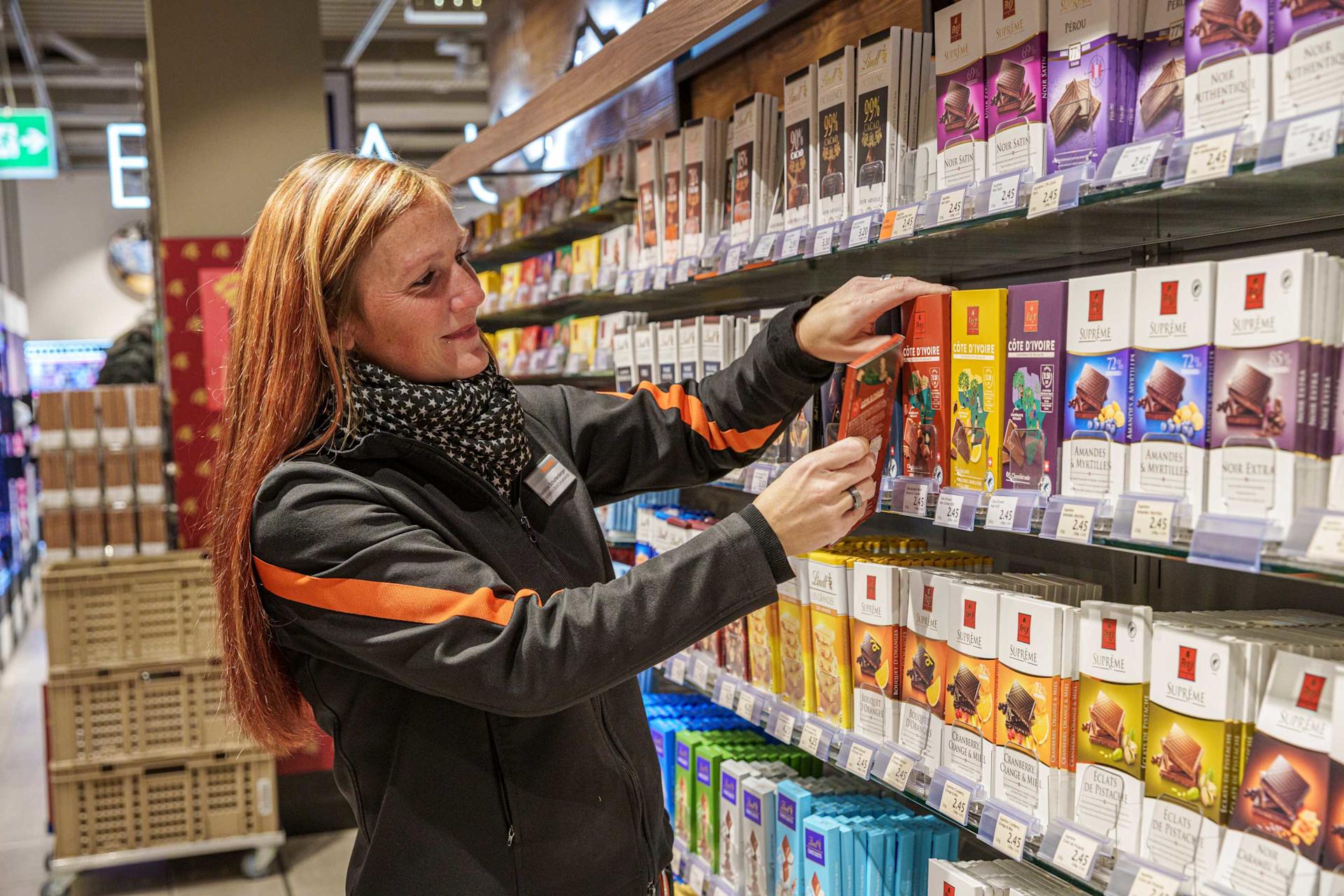 Une employée de Migros remplit un rayon de chocolat