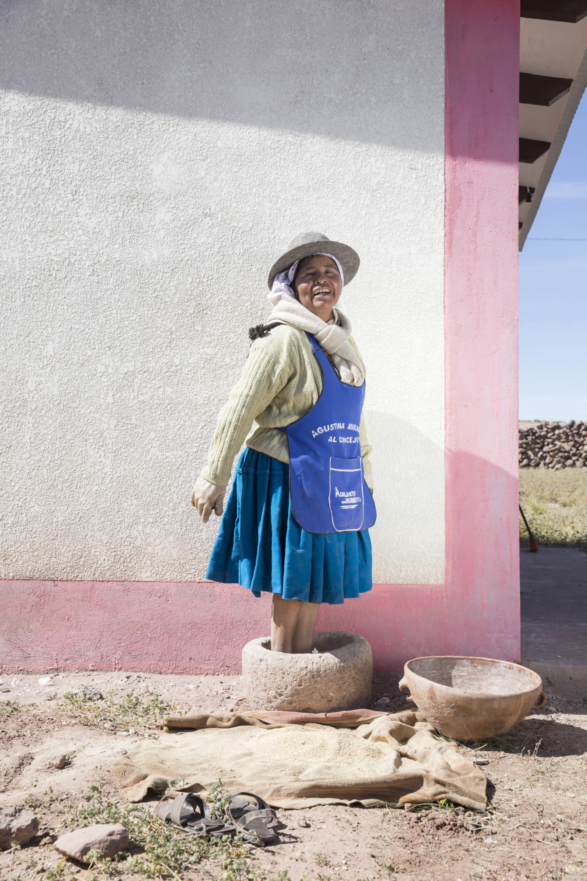 La cueilleuse et cuisinière Cecilia se tient devant un mur rose et rit devant la caméra.