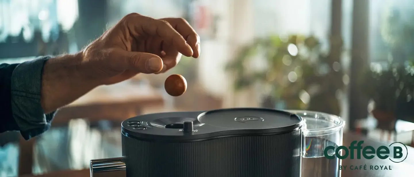 Eine Hand wirft einen Coffee Ball in eine Maschine.