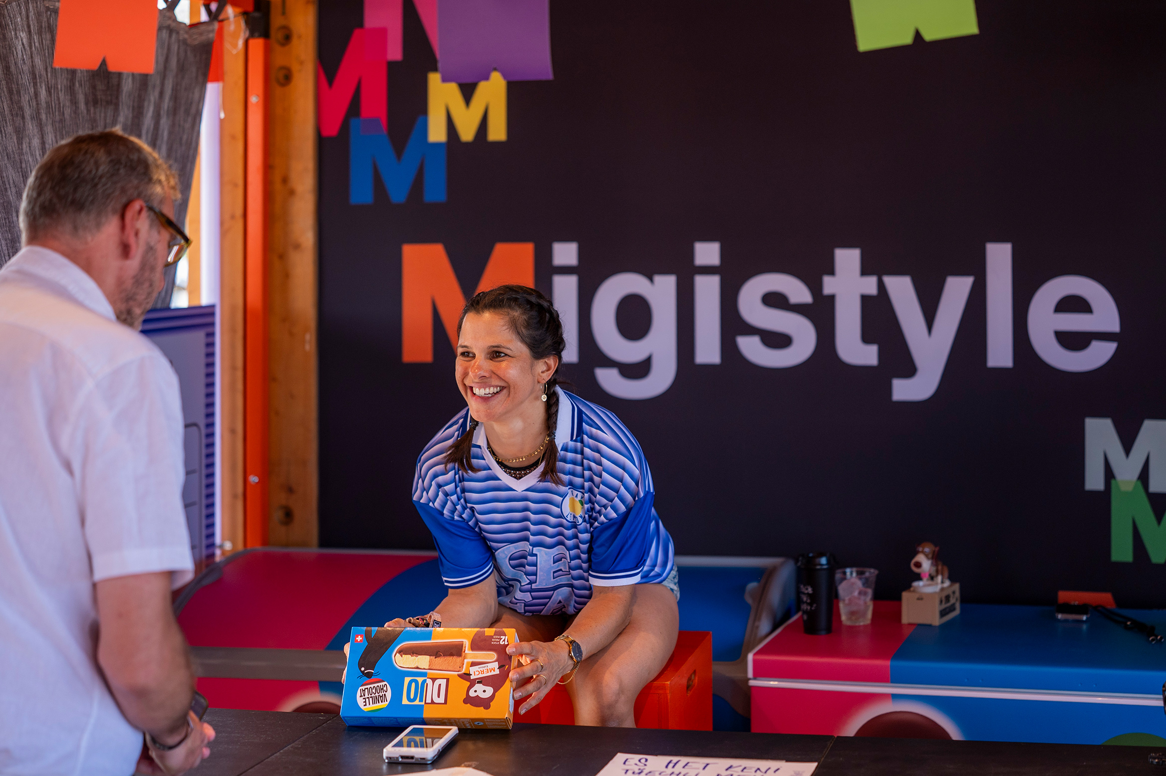 A young woman hands out Migros ice cream at a festival stand.