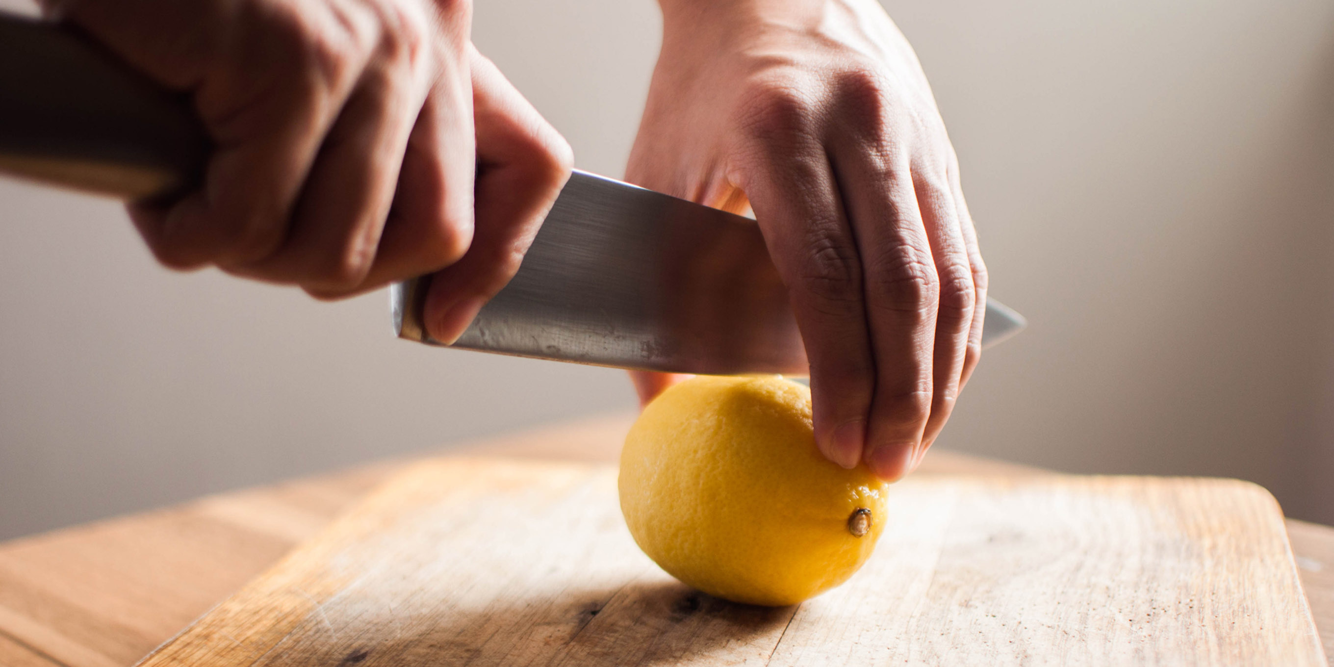 Un limone appoggiato su un tagliere viene tagliato con un grosso coltello.