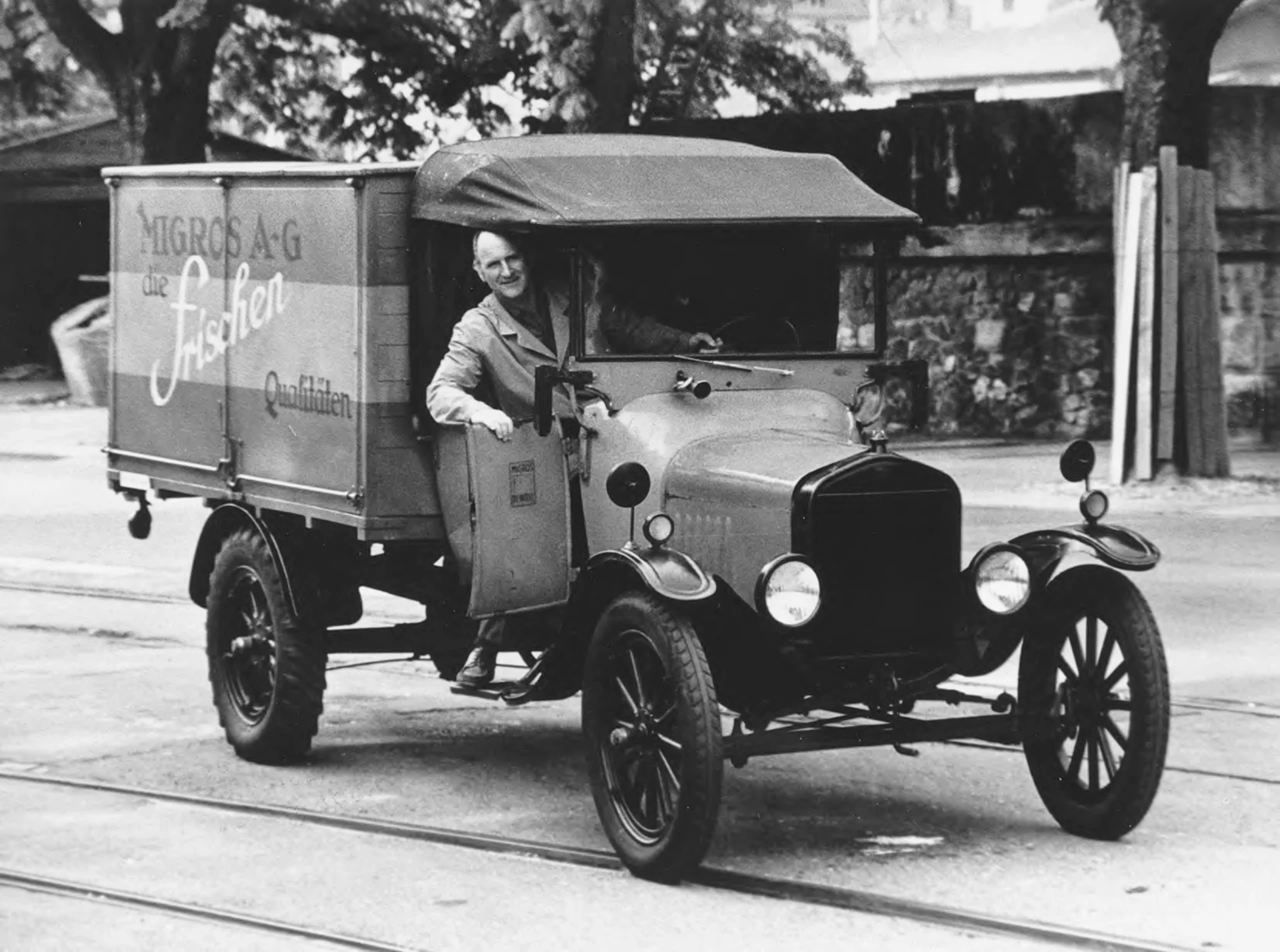 Eine Schwarz-Weiss-Fotografie eines Migros-Verkaufswagens mit Chauffeur.