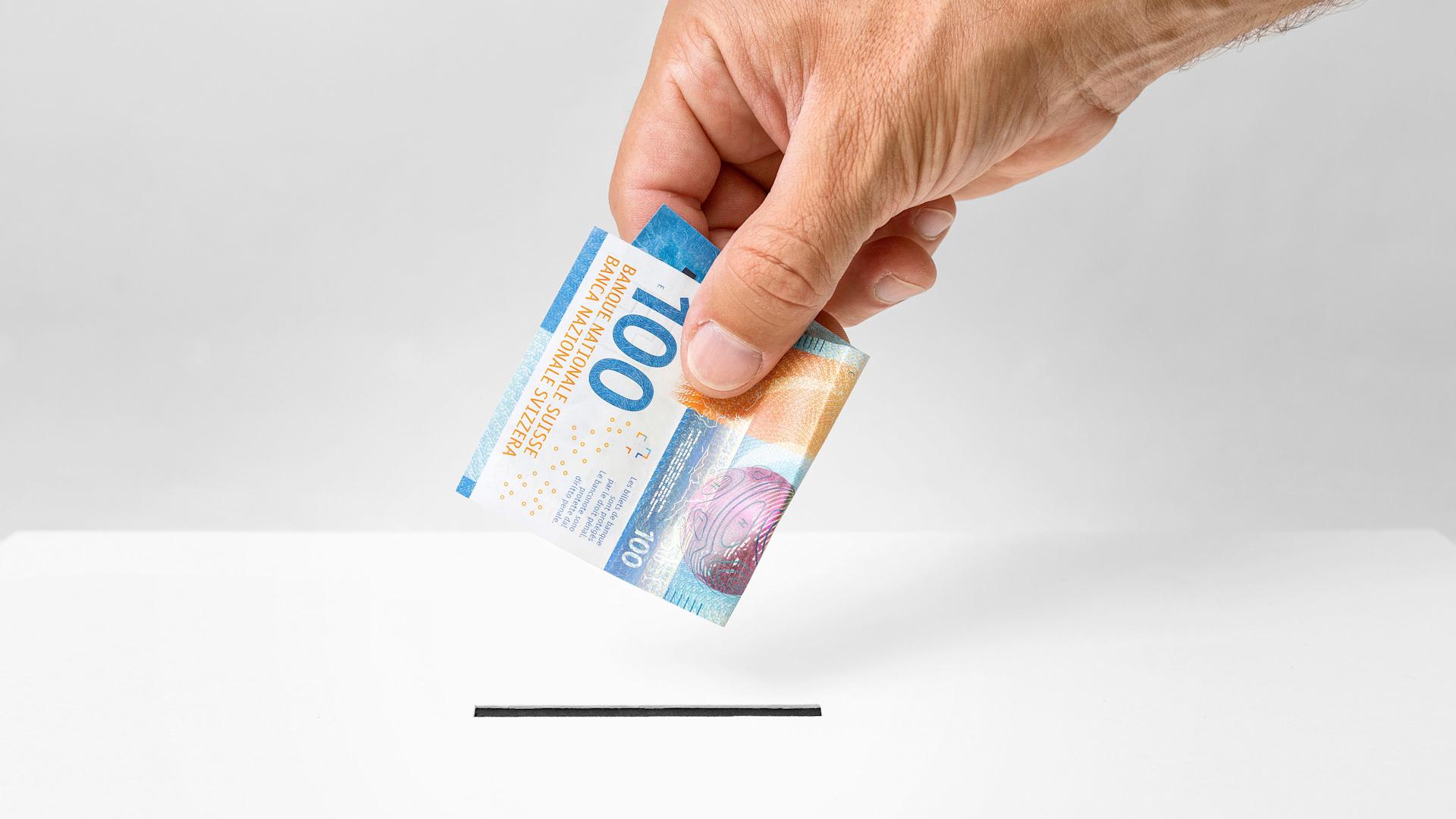 Une main d'homme glisse cent francs dans une boîte