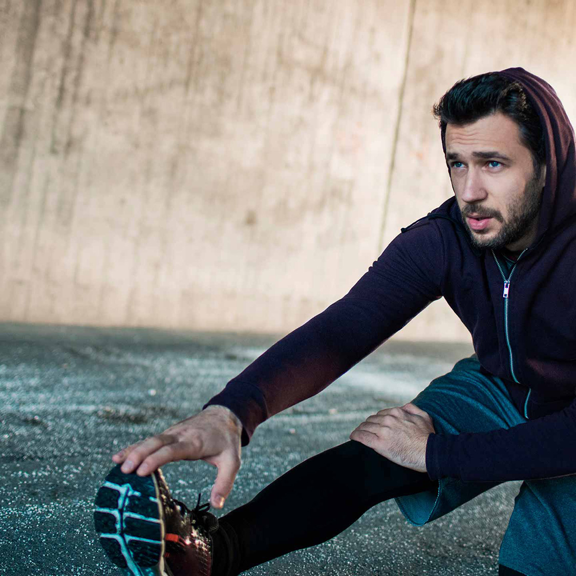 Ein junger Mann macht in einer Unterführung Dehnübungen.