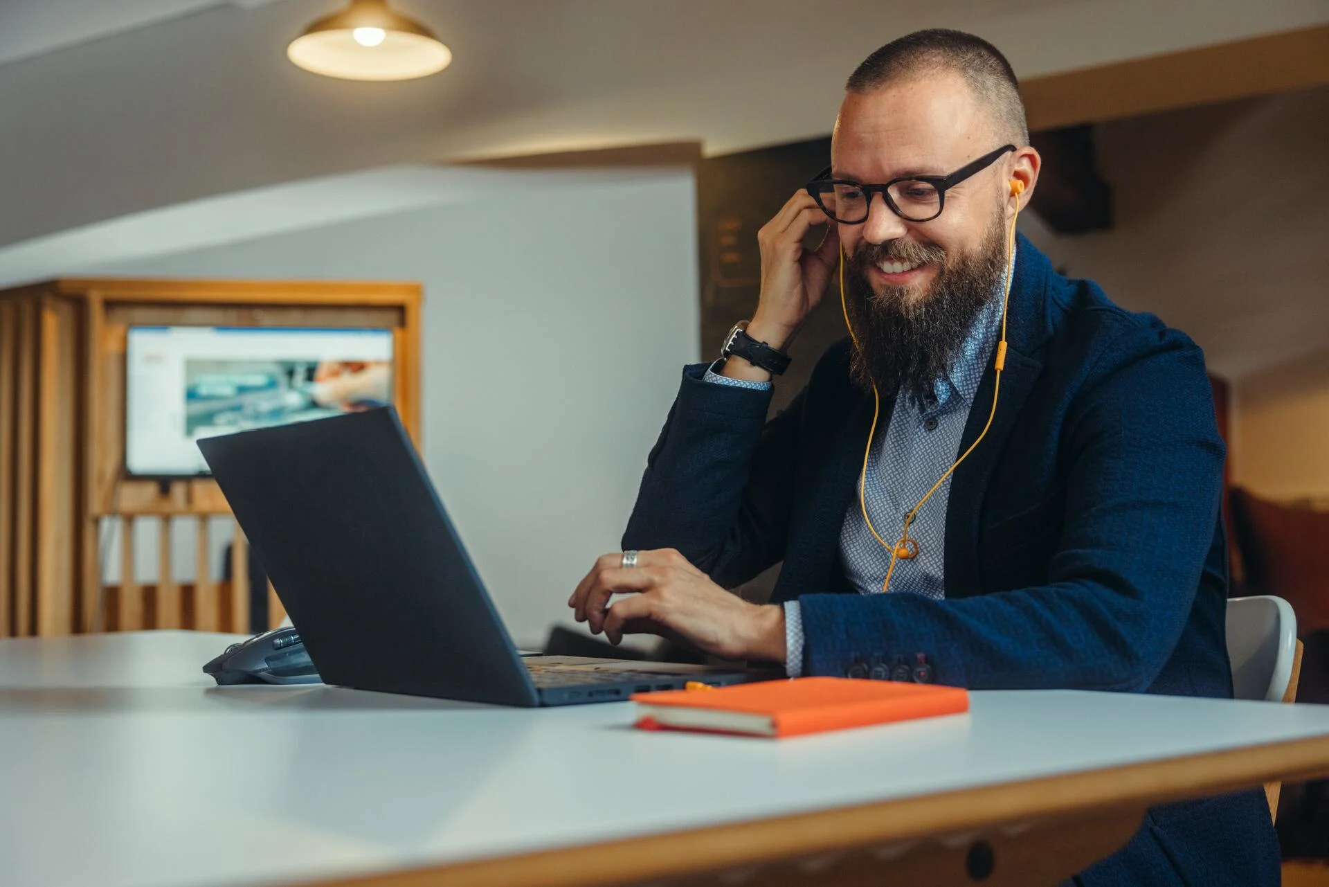 Un uomo con barba e occhiali partecipa a una telefonata in un ufficio davanti al suo computer portatile.