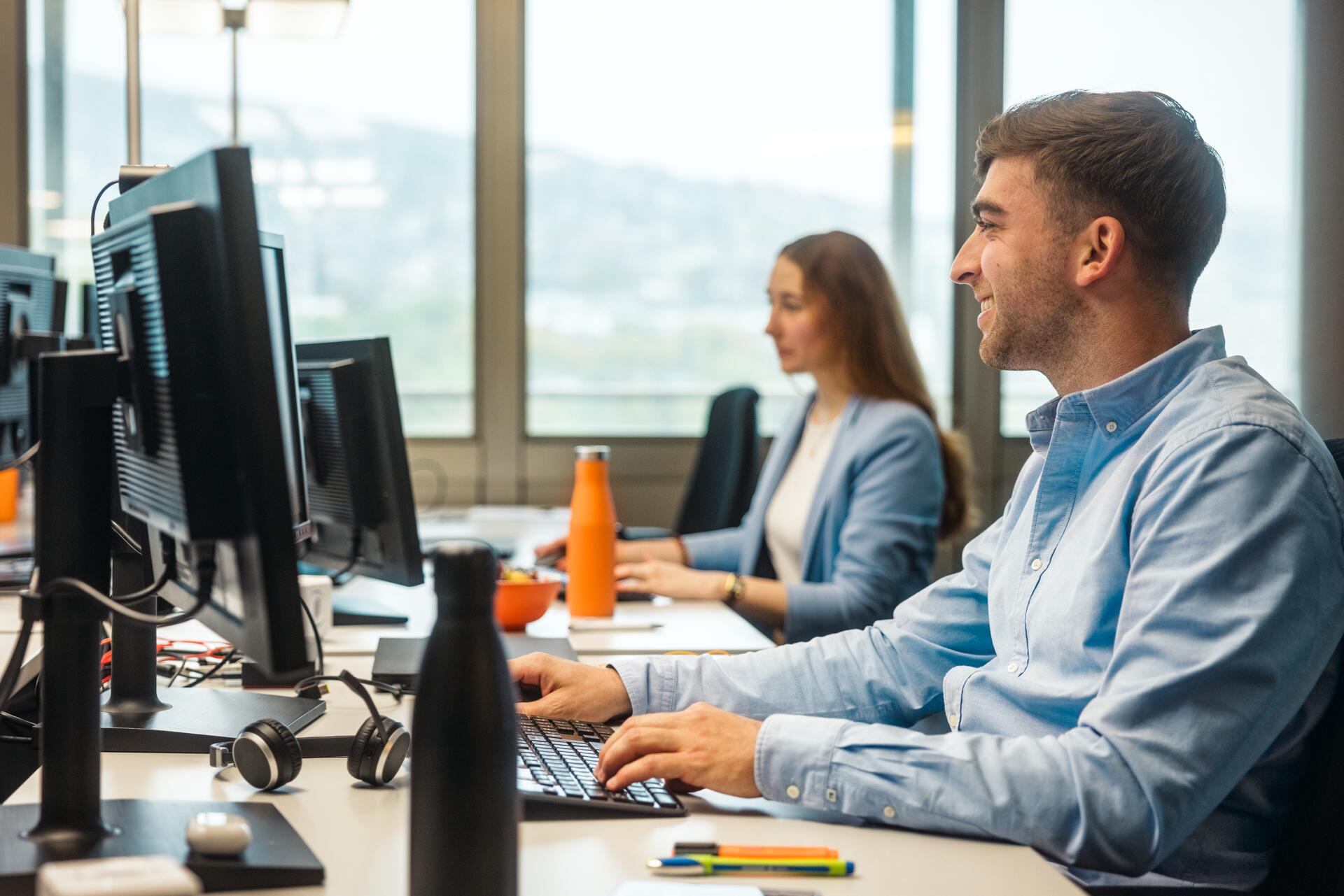 Zwei Migros-Mitarbeitende arbeiten in einem Büro vor ihren Bildschirmen.
