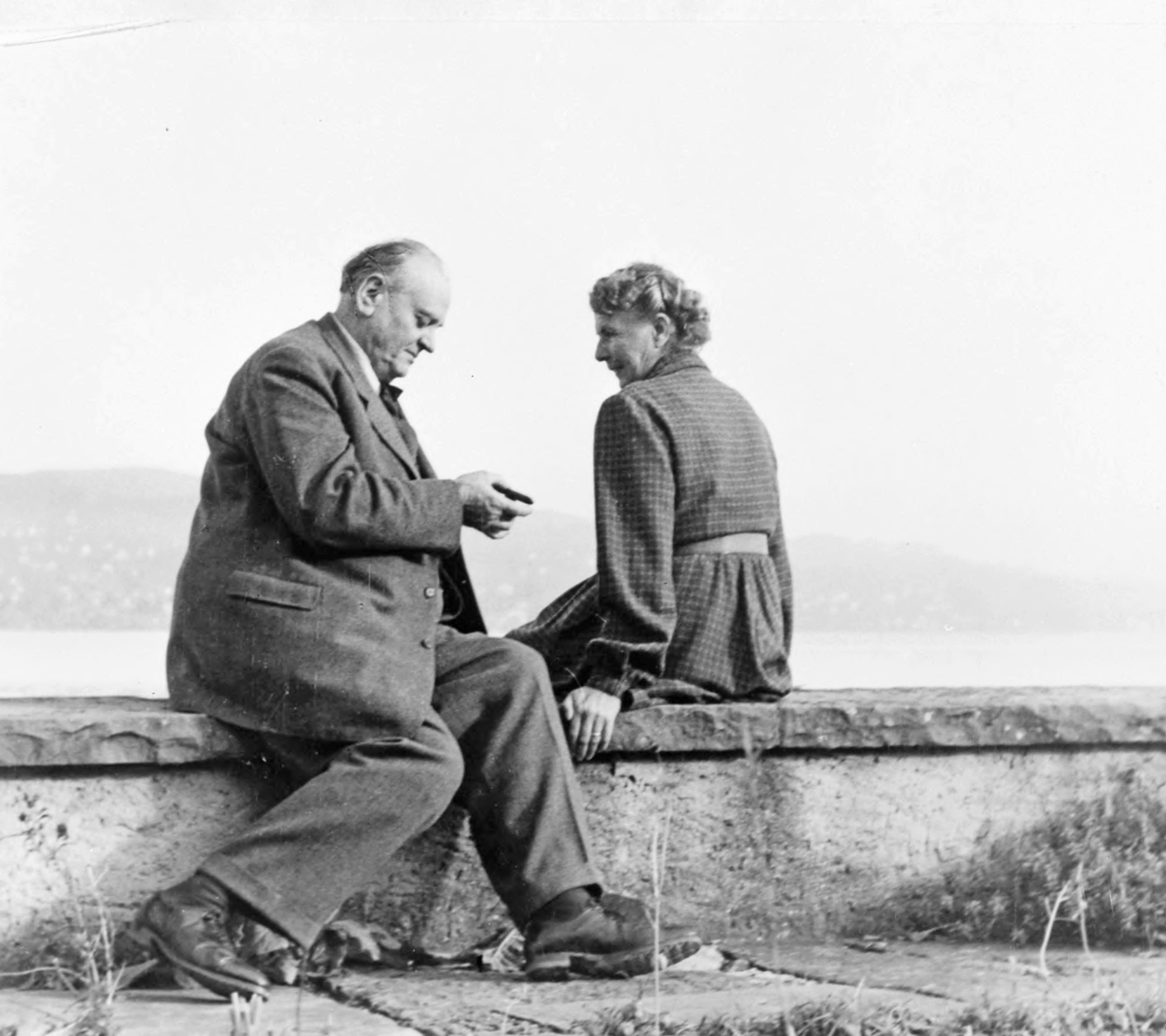 Eine Schwarz-Weiss-Fotografie von Gottlieb und Adele Duttweiler, sitzend auf einer Mauer am Zürichsee.