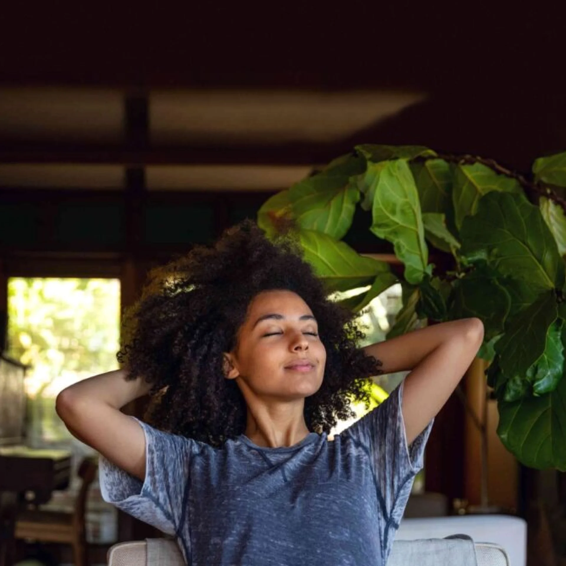 A woman relaxes in an armchair next to a plant