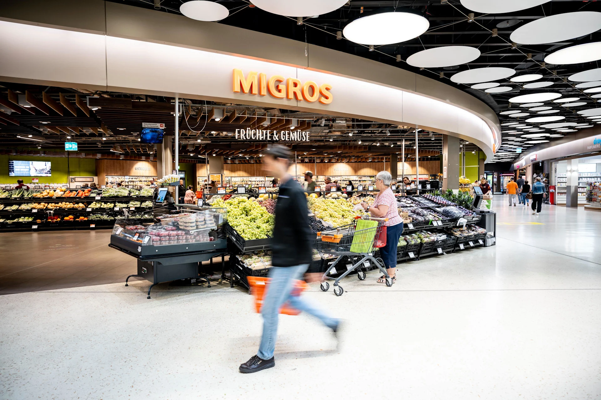 Eine Kundin und ein Kunde vor dem Eingang der Filiale Migros Surseepark