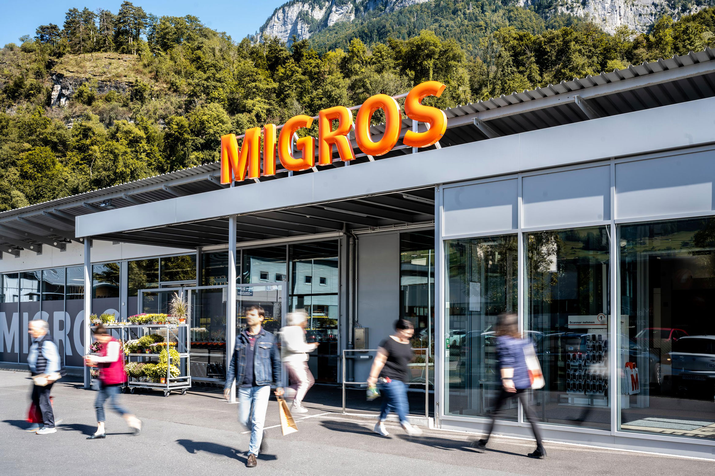 Kunden vor dem Eingang einer modernen Migros Filiale