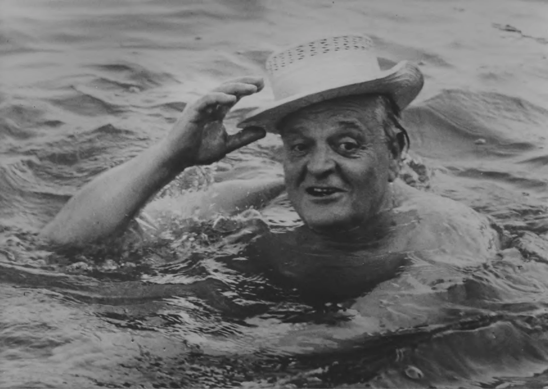 Una fotografia in bianco e nero di Gottlieb Duttweiler. Dutti nuota nell'acqua e indossa un cappello di paglia