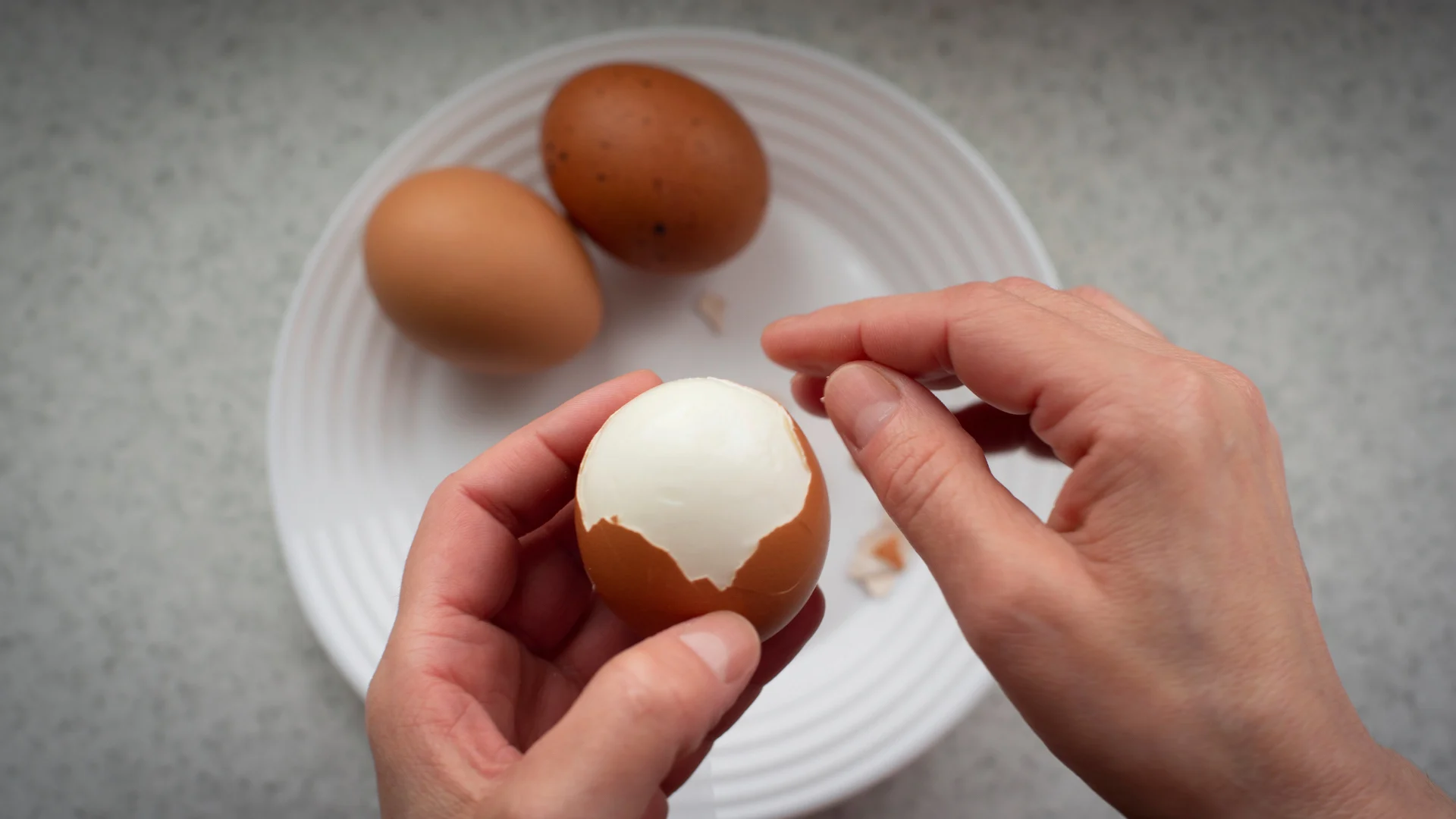 Eine Hand hält ein hartgekochtes Ei, während mit der anderen Hand das Ei geschält wird.