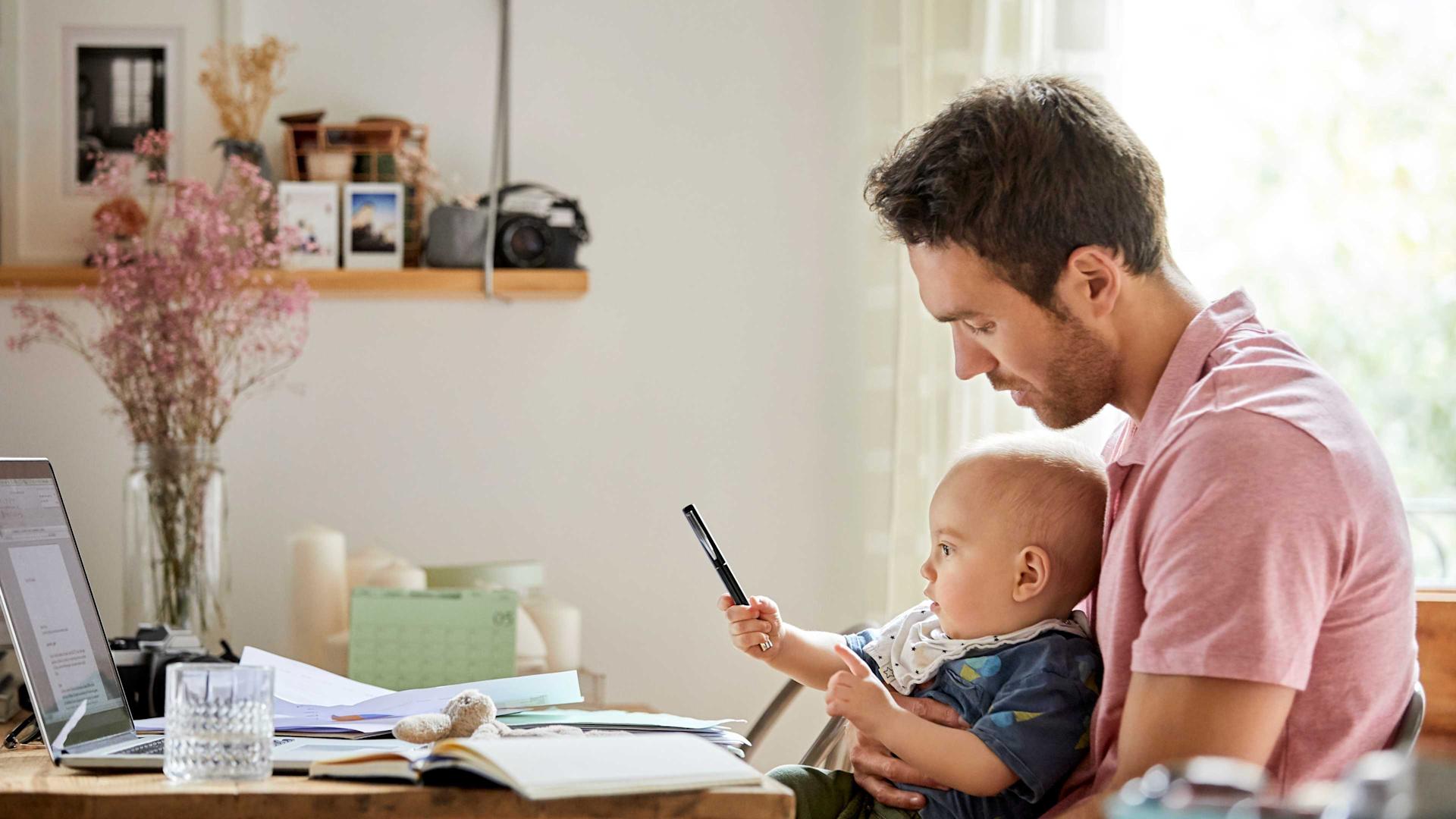 Vater betrachtet seinen kleinen Jungen, der mit einem Stift spielt, während er an einem Schreibtisch sitzt