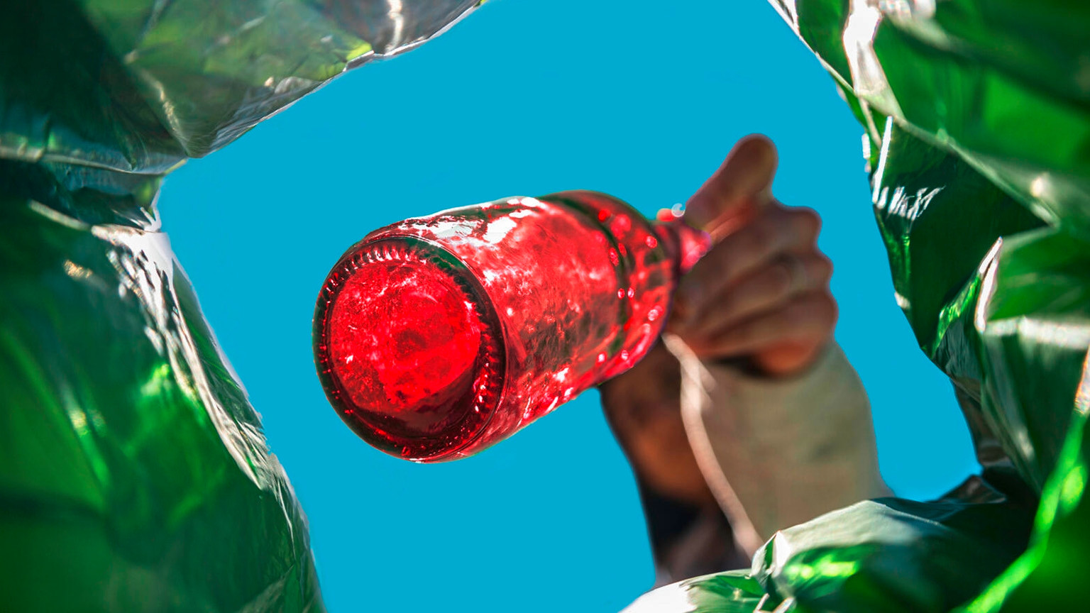 Une main tient une bouteille rouge au-dessus d’une poubelle