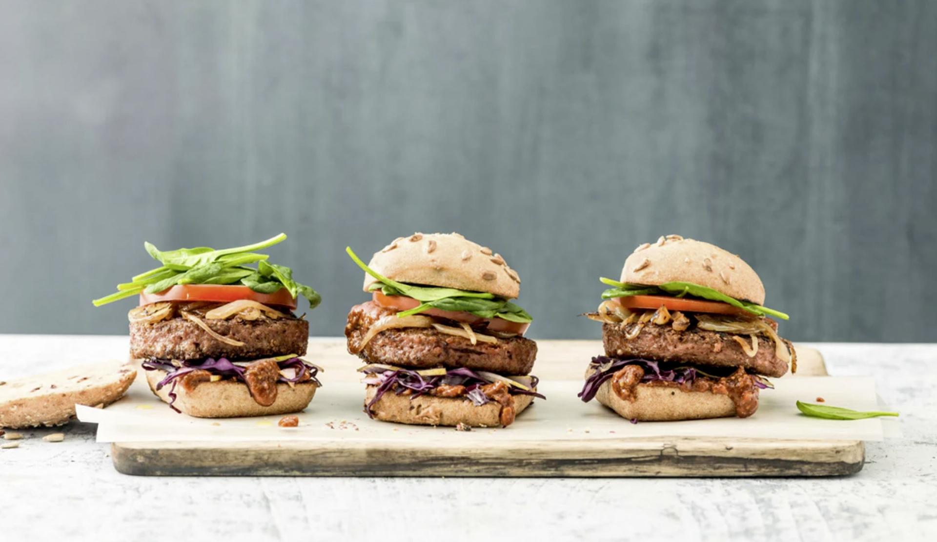 Three vegan burgers on a wooden board
